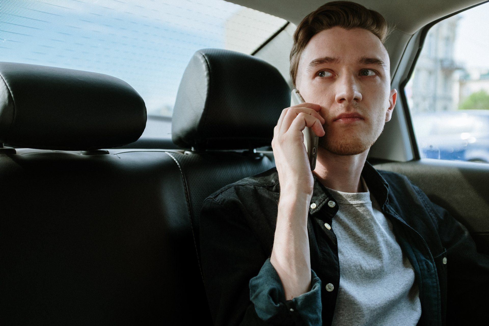 Man sitting in the back seat of a car, holding a phone to his ear and looking out the window.