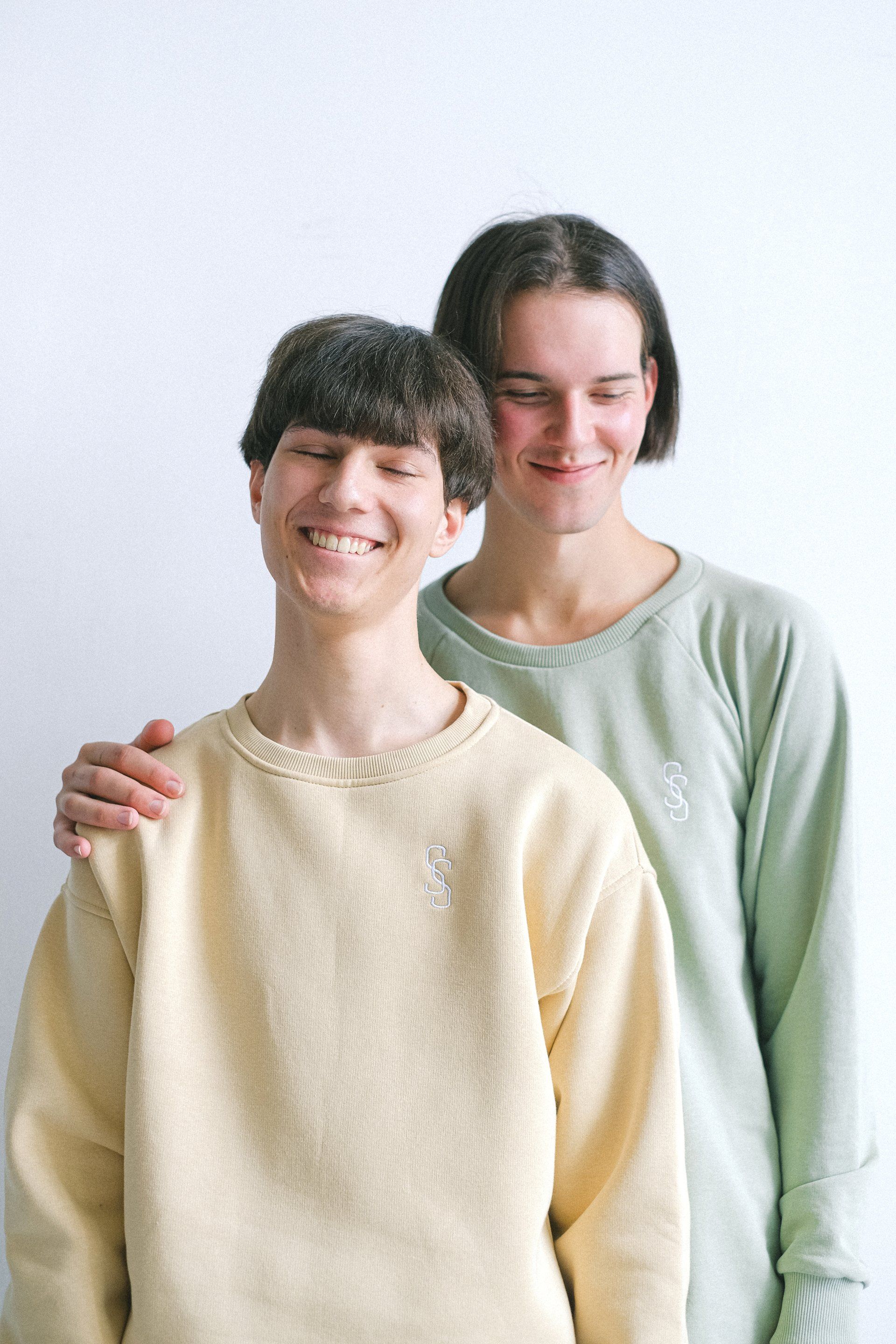 Two young men in sweaters are standing next to each other and smiling.