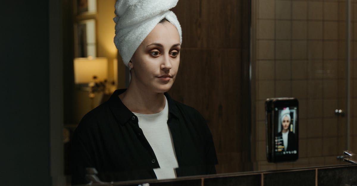 A woman with a towel wrapped around her head is looking at herself in the mirror.