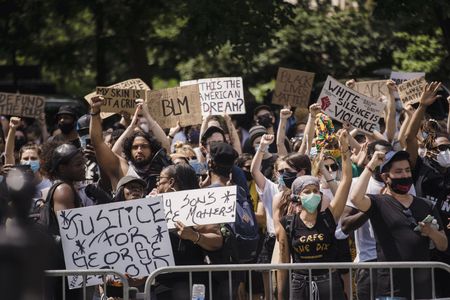 Protesters holding signs and raising fists behind a barricade on a city street.