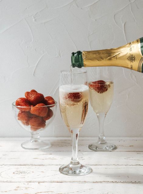 Champagne poured into fluted glasses with strawberries. A glass bowl holds more strawberries; bright setting.