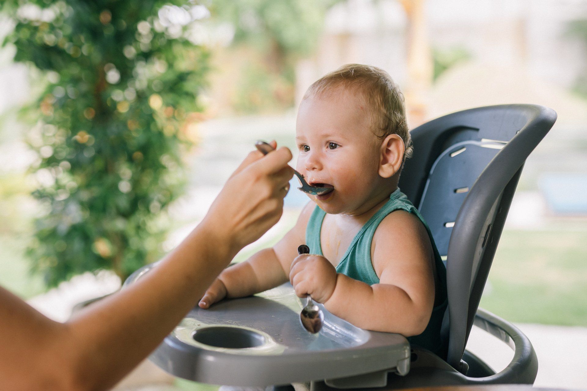 A woman is feeding a baby in a high chair with a spoon.