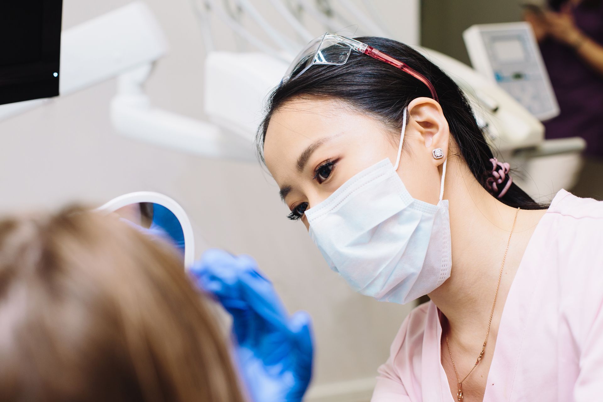 a female dentist wearing a mask and goggles examines a patient 's teeth