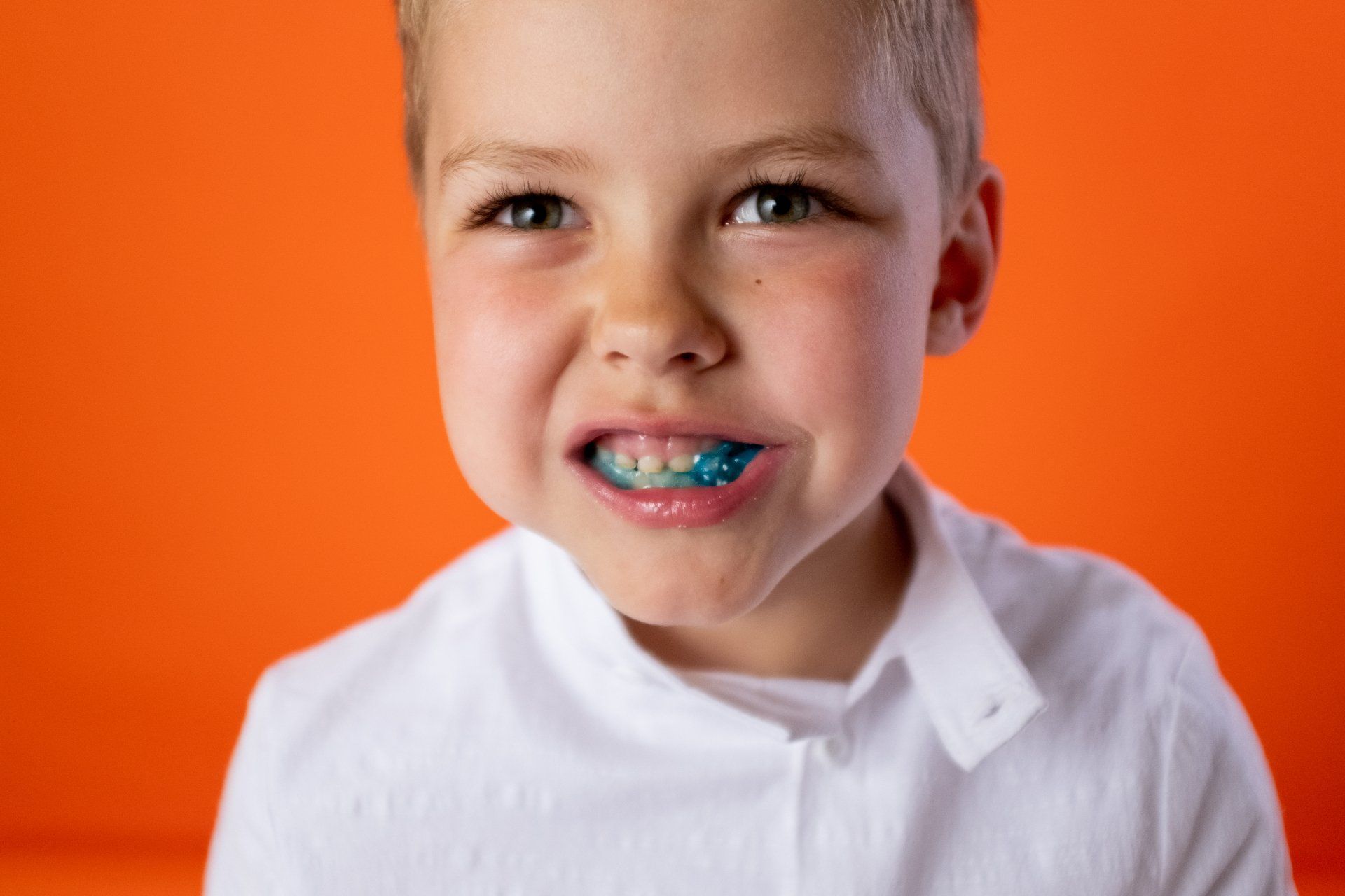 Boy wearing blue mouthguard, orange backdrop.