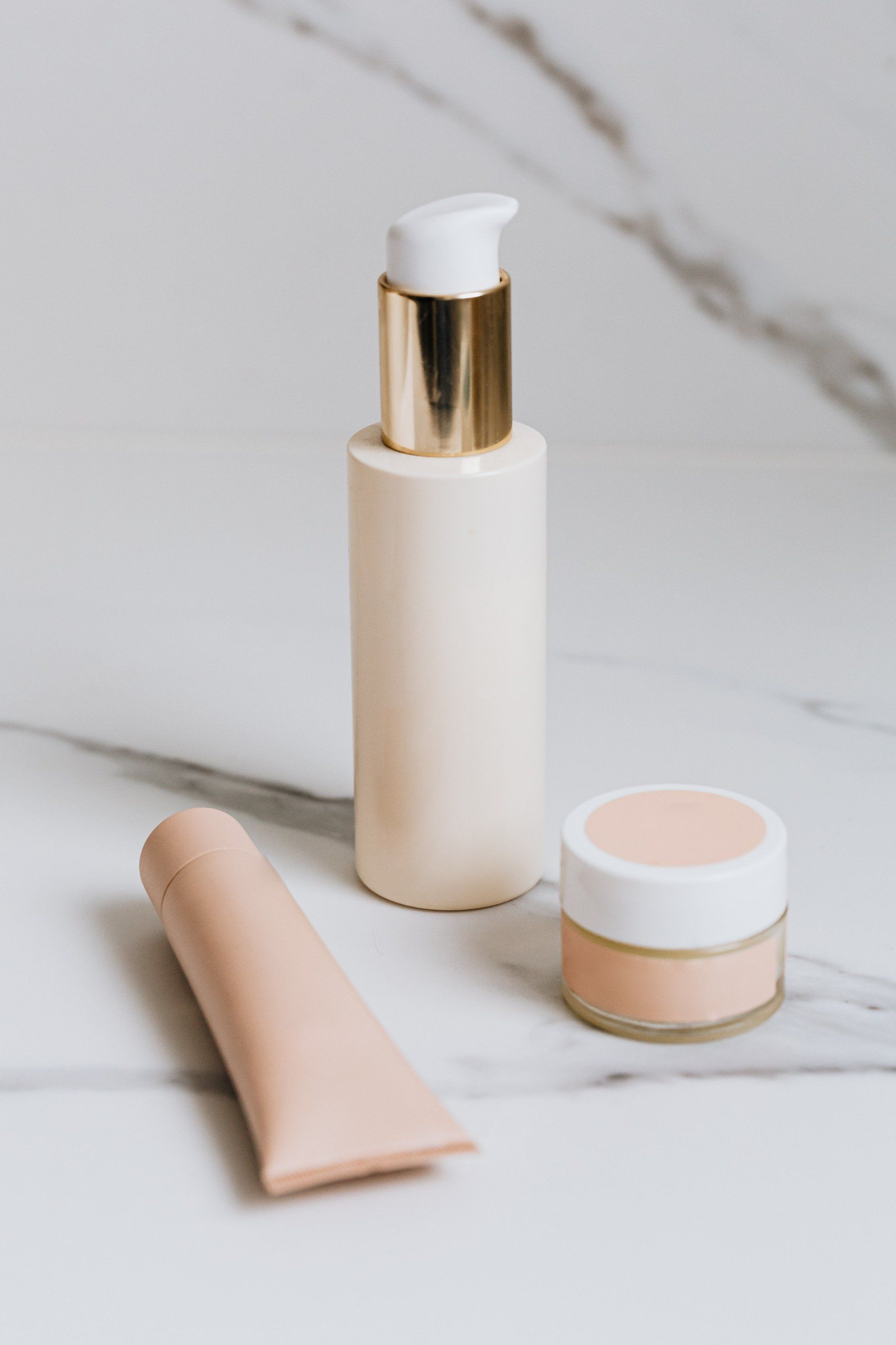 A bottle of lotion , a tube of cream , and a jar of powder are on a table.