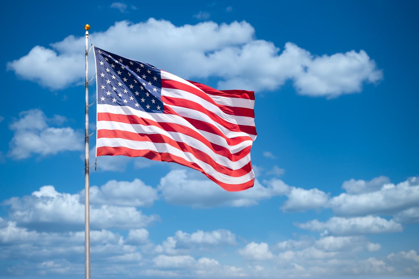 American flag waving in front of a blue sky with white clouds.