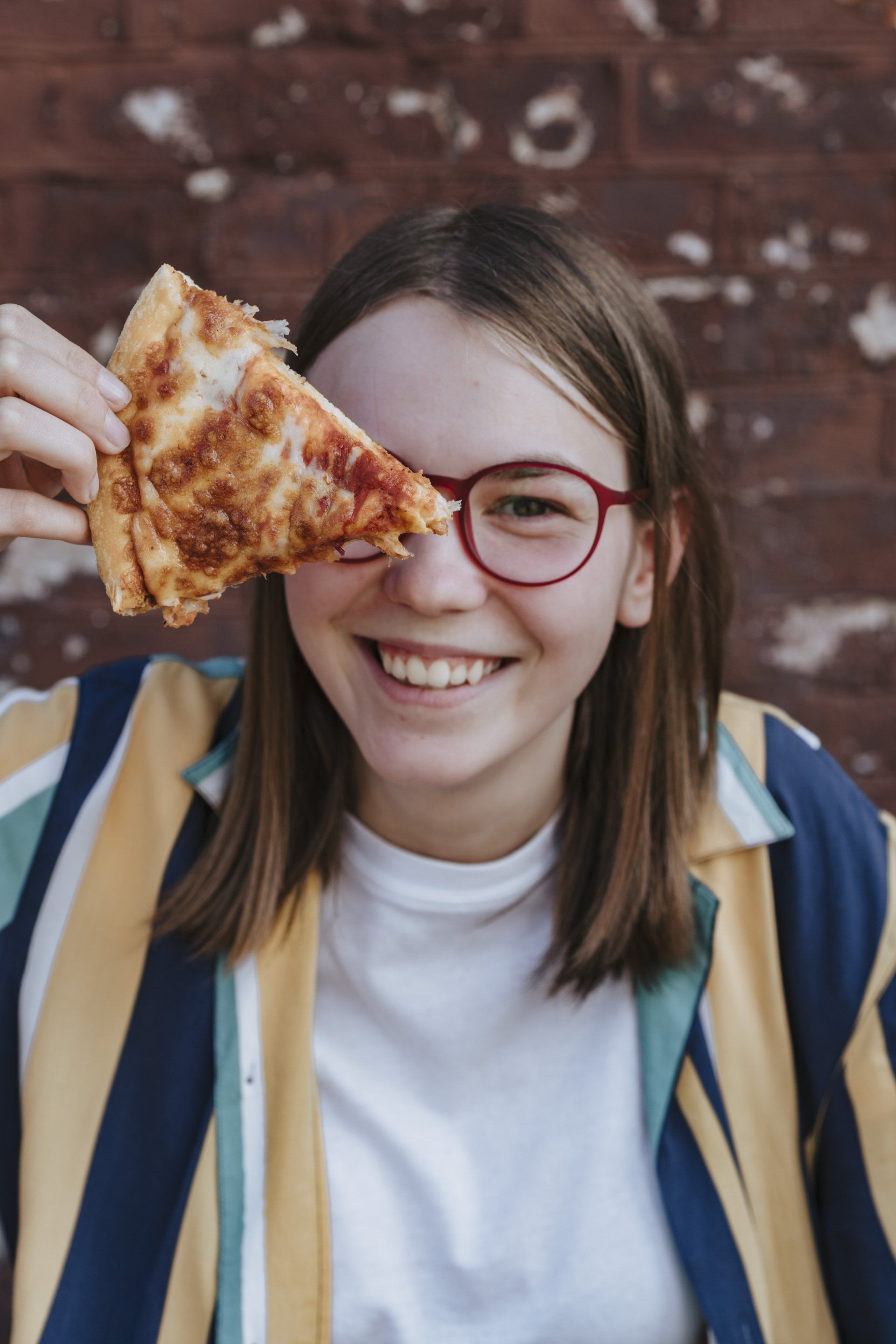A young woman is holding a slice of pizza in front of her eye.