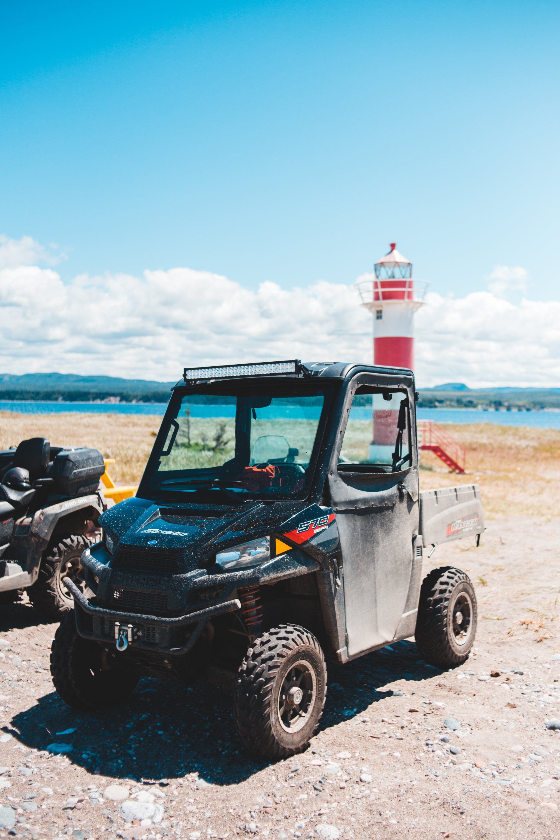Black utility vehicle parked near a red and white lighthouse on a sunny day.