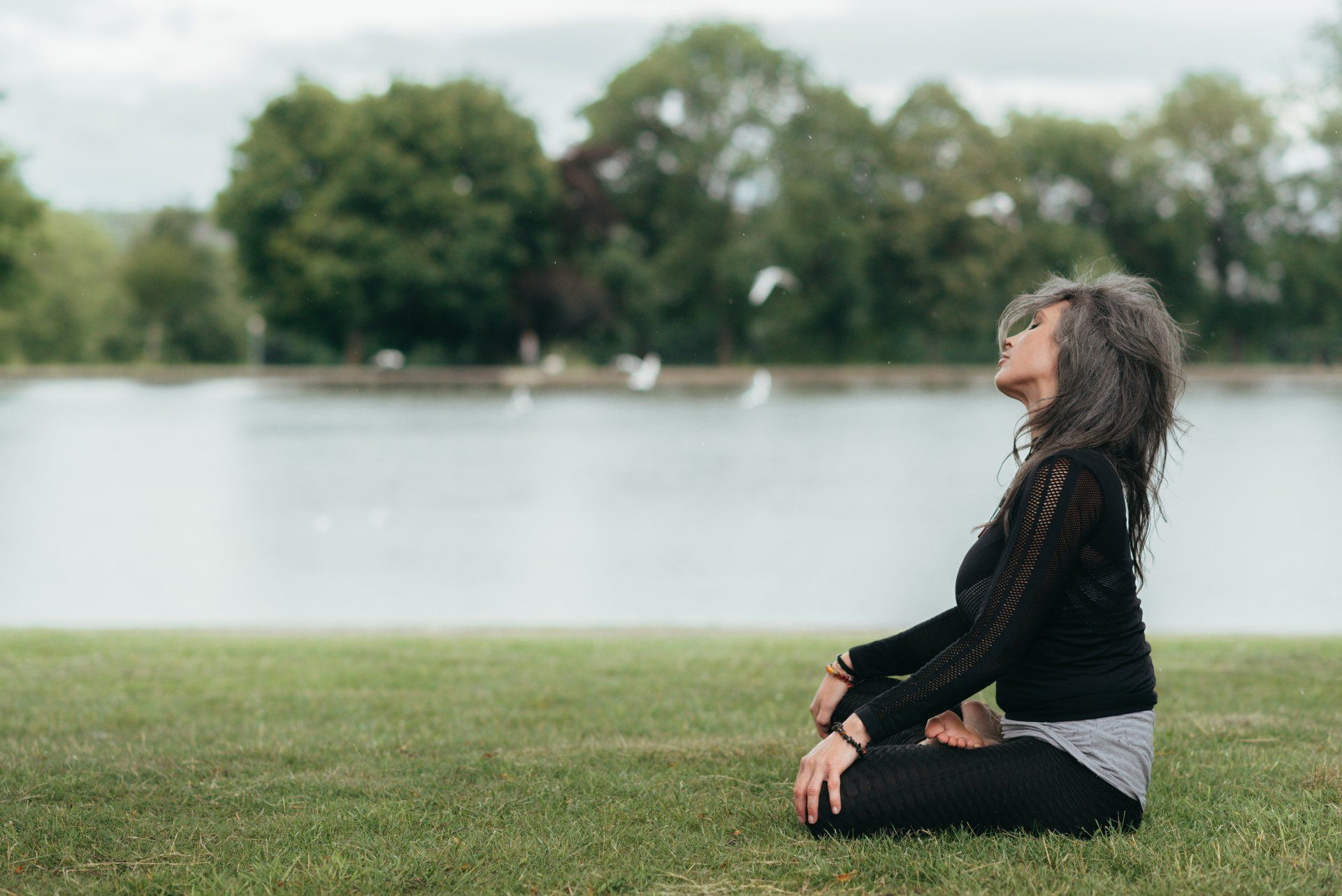 A woman is sitting on the grass in front of a lake.