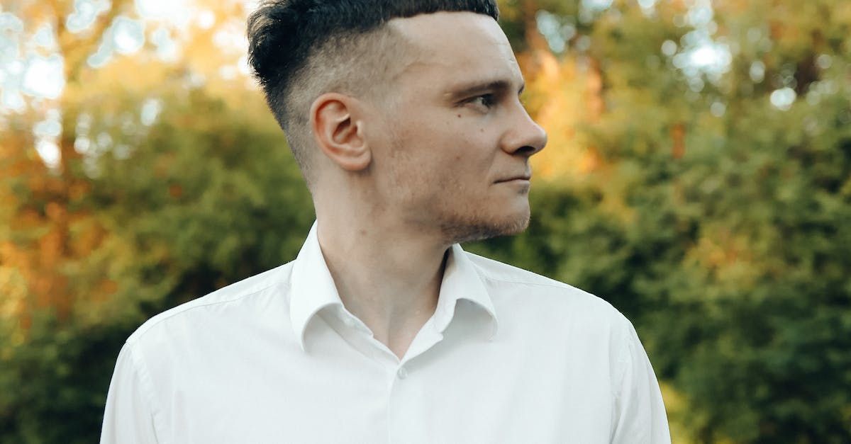 A man in a white shirt is standing in front of a forest.