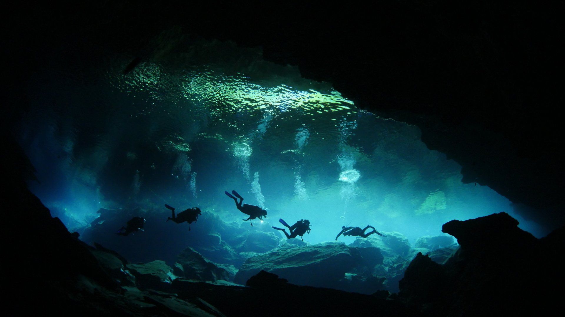 A group of scuba divers are swimming in a cave.