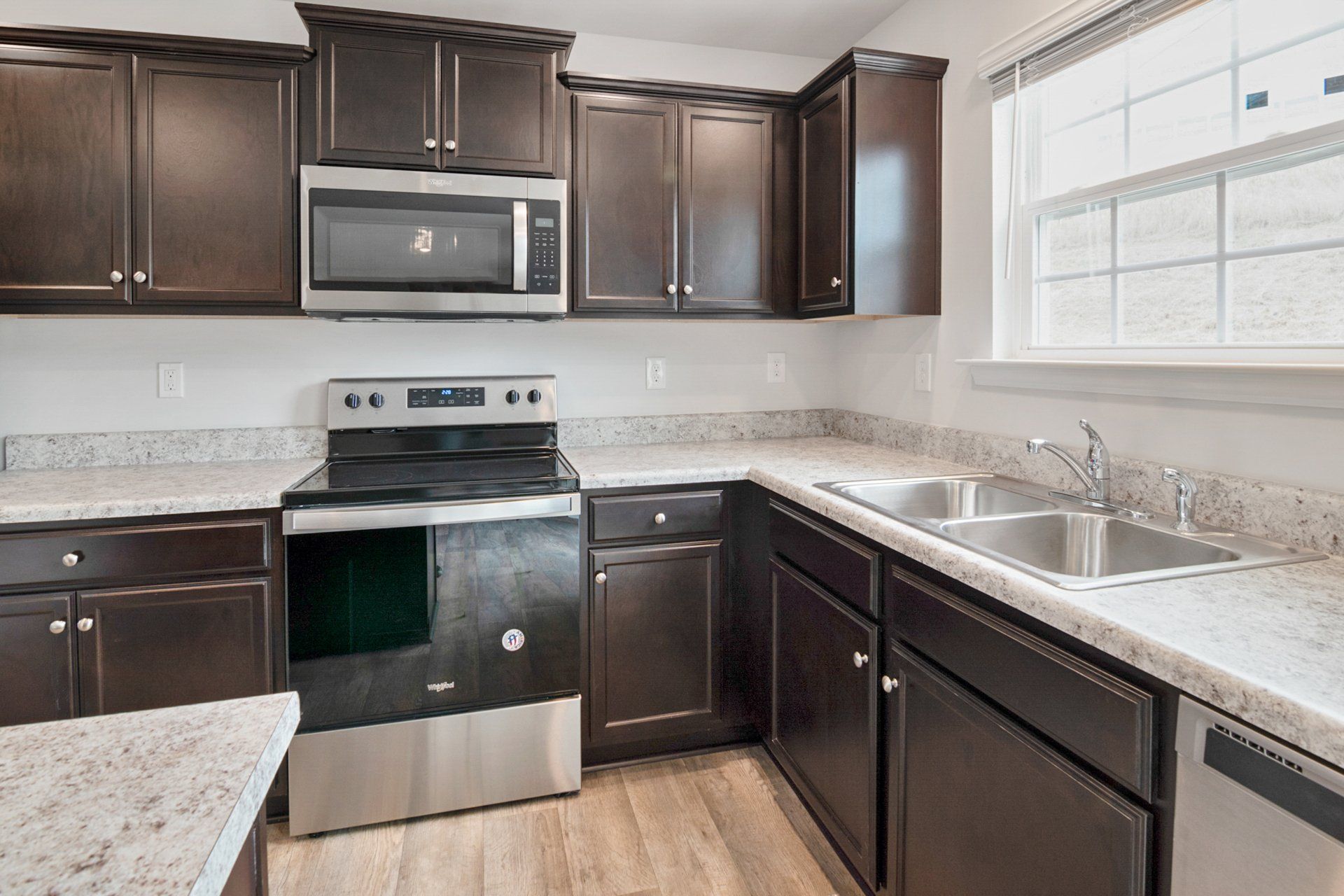 A kitchen with stainless steel appliances , wooden cabinets , granite counter tops and a window.