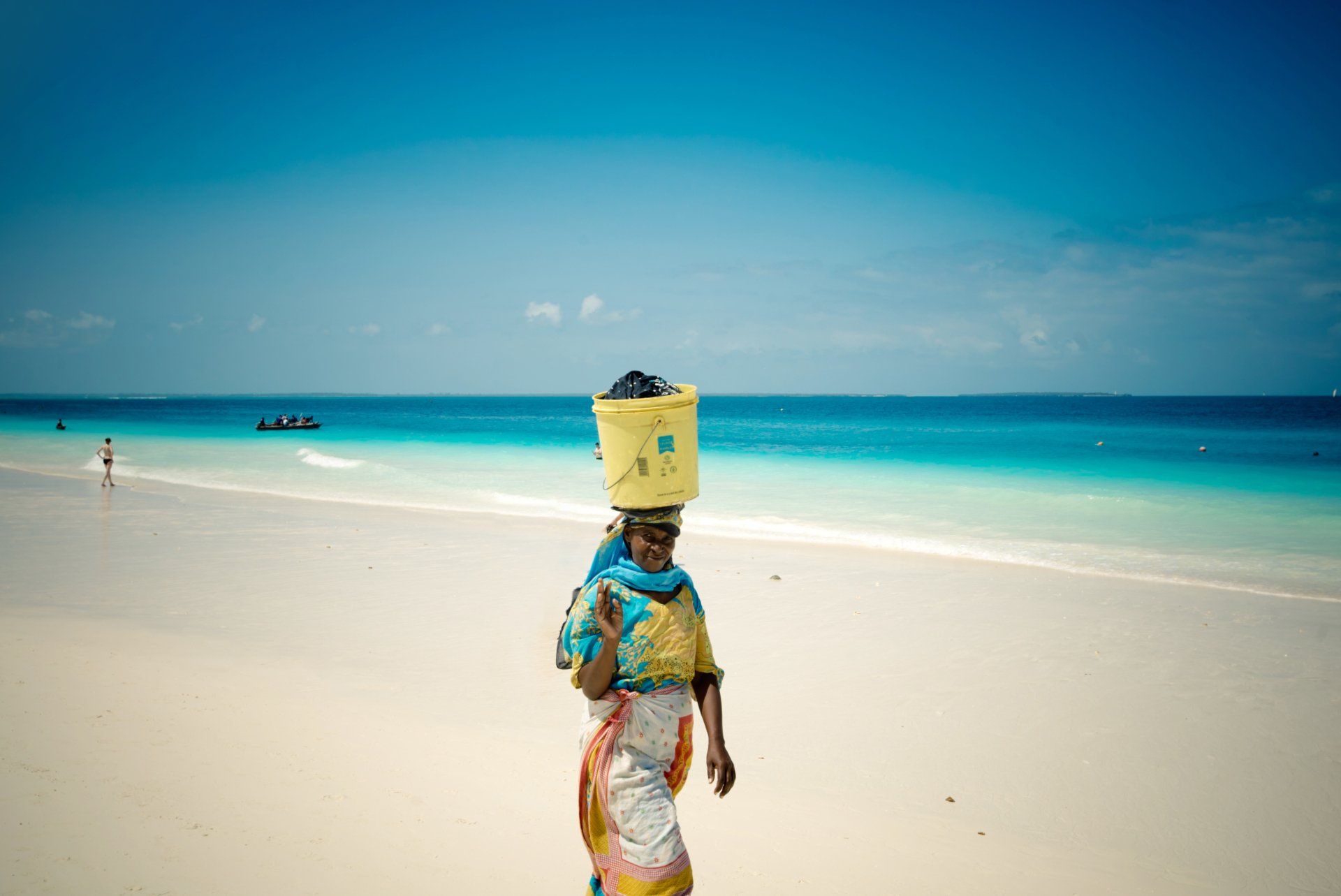 A woman is walking on a beach with a bucket on her head.