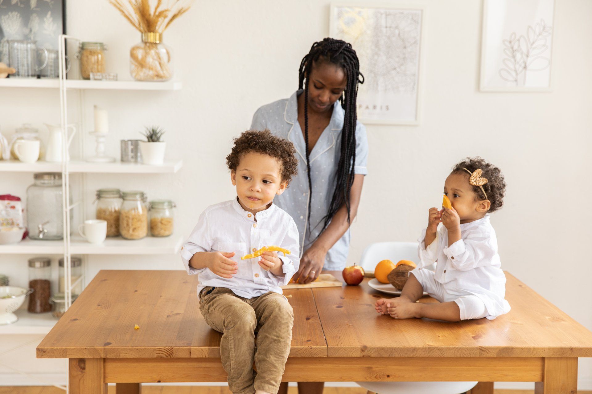 A woman and two children are sitting at a table eating fruit.