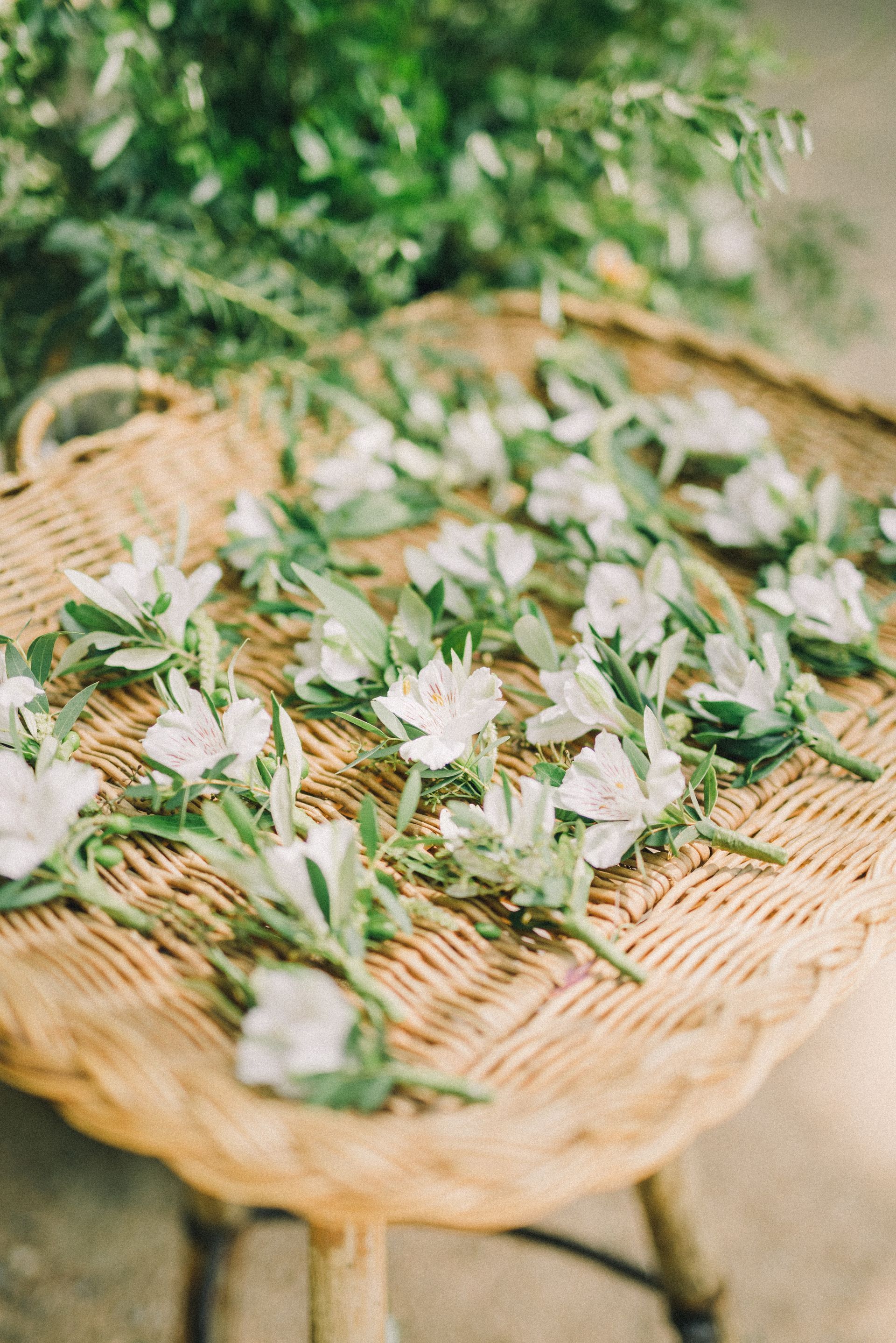 Een rieten mand gevuld met witte bloemen en groene bladeren.