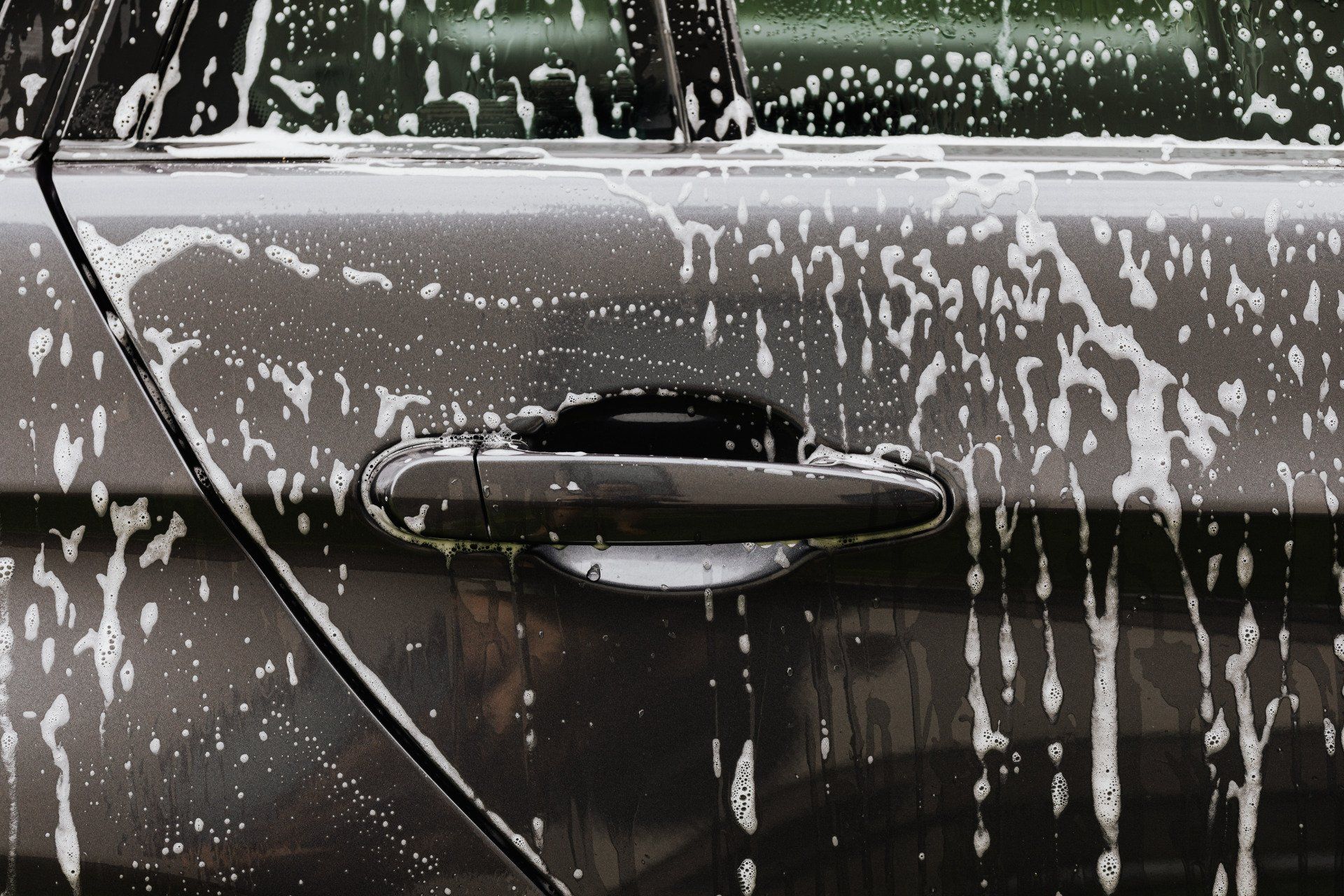 Car door covered in white soap suds during a car wash