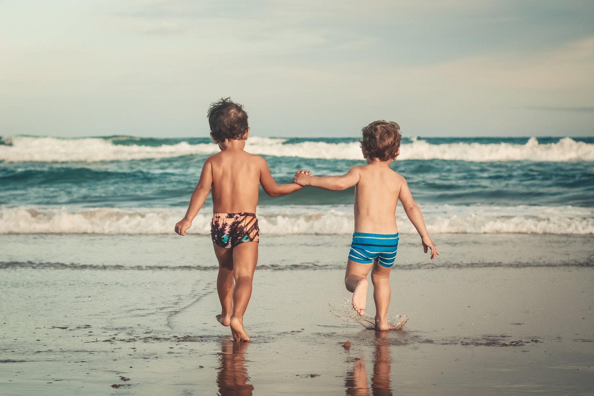 Two kids running into ocean holding hands Fusion Partners Central Coast
