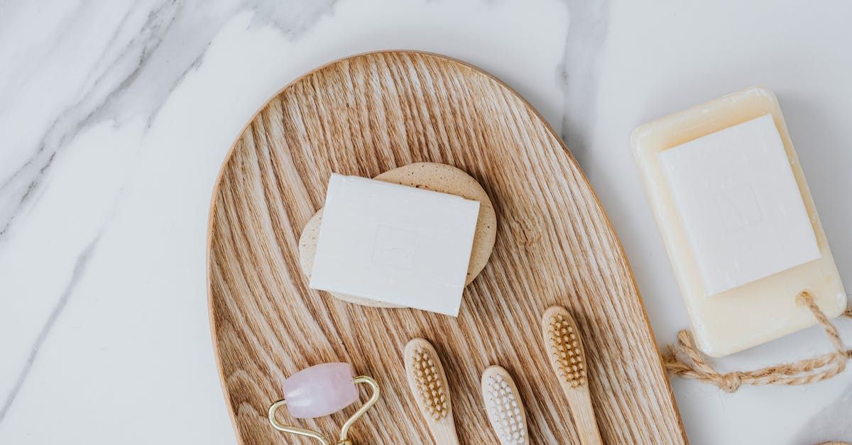 Bath accessories on a woven tray with soap bars, brushes, and a pale candle on a marble surface.