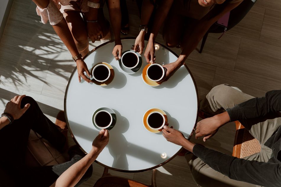 Six people sit around a round table, each holding a coffee cup from an overhead view.