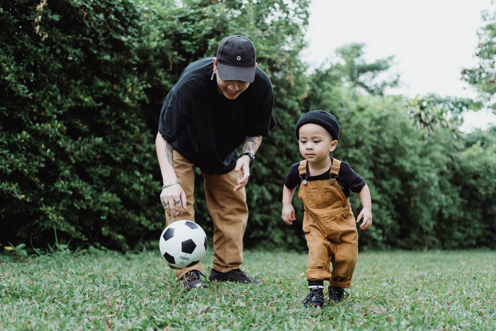 A man and a little boy are playing with a soccer ball in the grass.