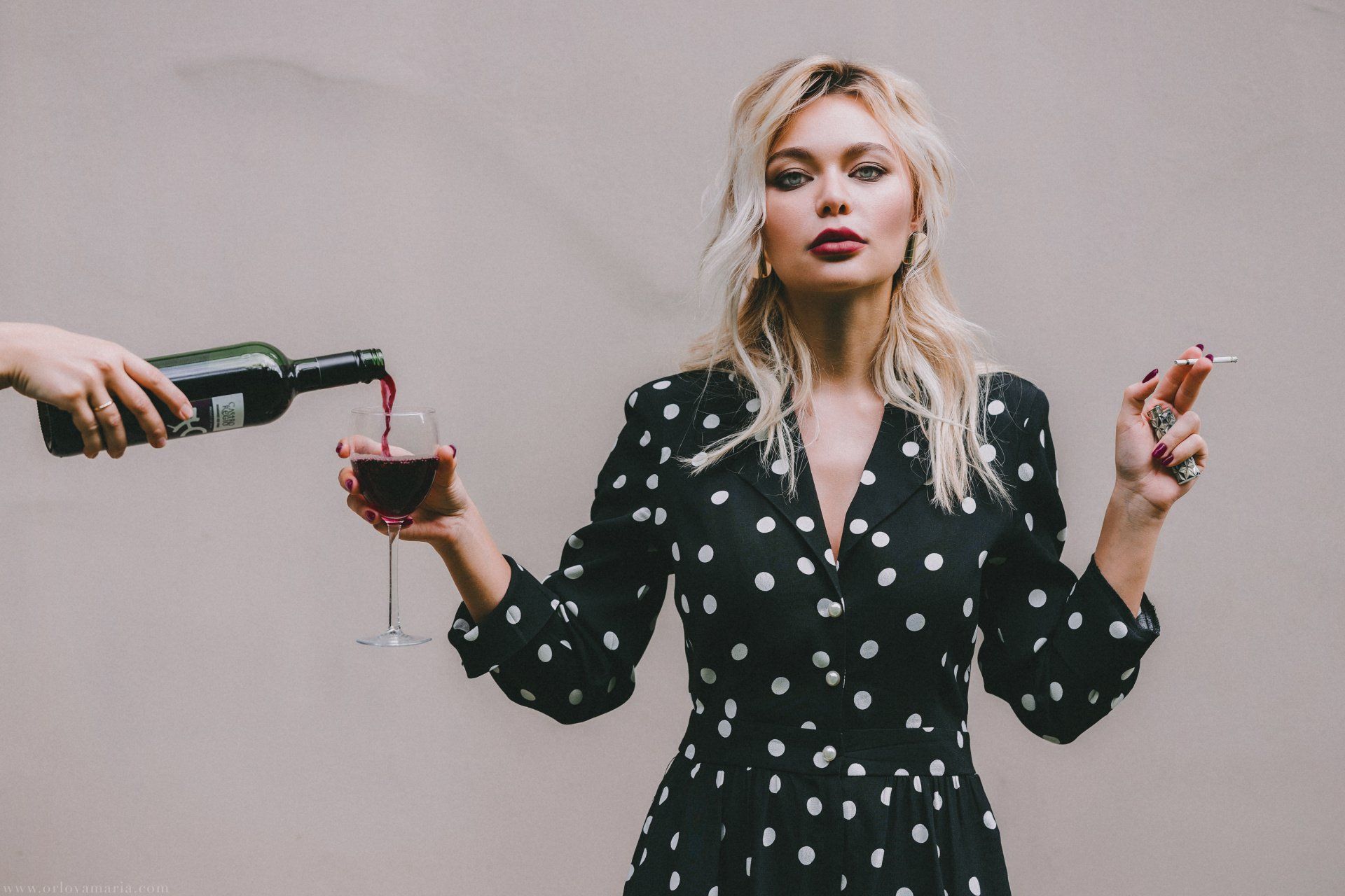 a woman in a polka dot dress holds a glass of wine and a bottle of wine