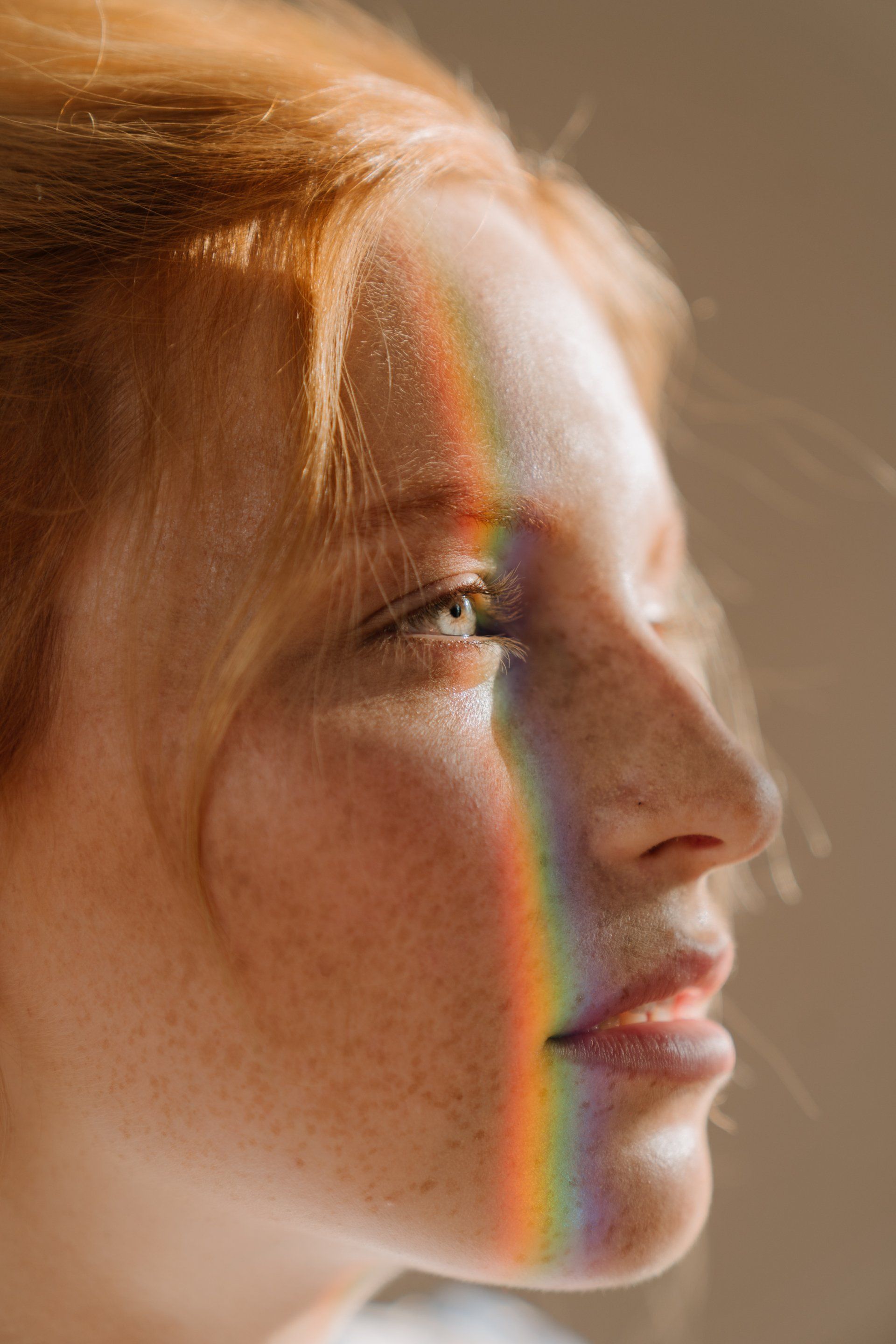 Close-up side profile of a woman in warm light, with a rainbow reflection across her face