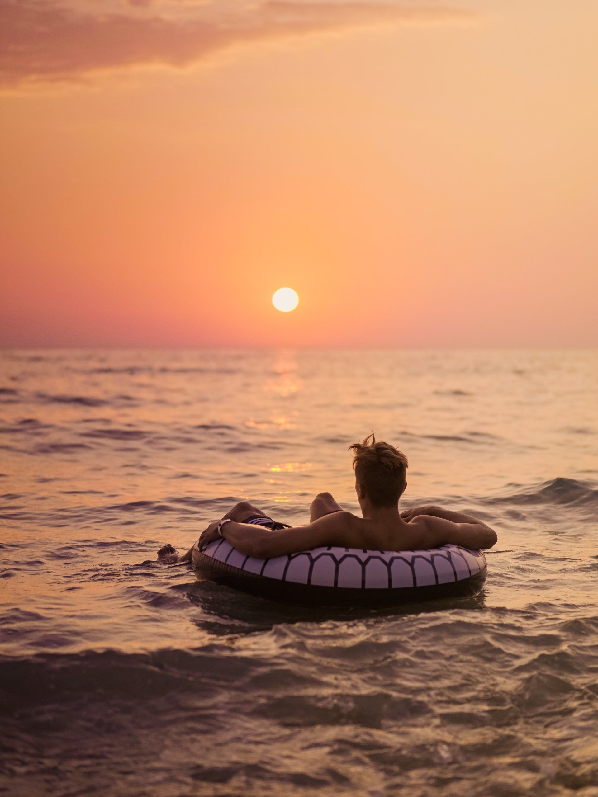 Ein Mann treibt bei Sonnenuntergang auf einem Schlauchboot im Meer.