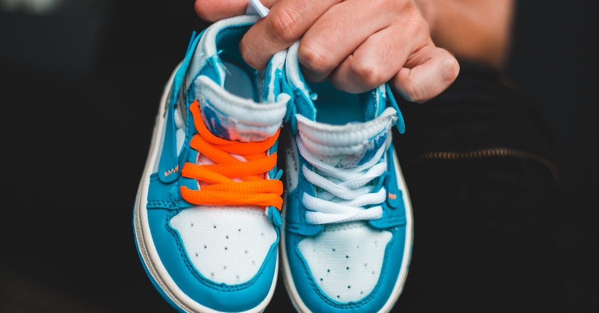 Person holding a pair of baby blue and white sneakers; one with orange laces, the other with white.