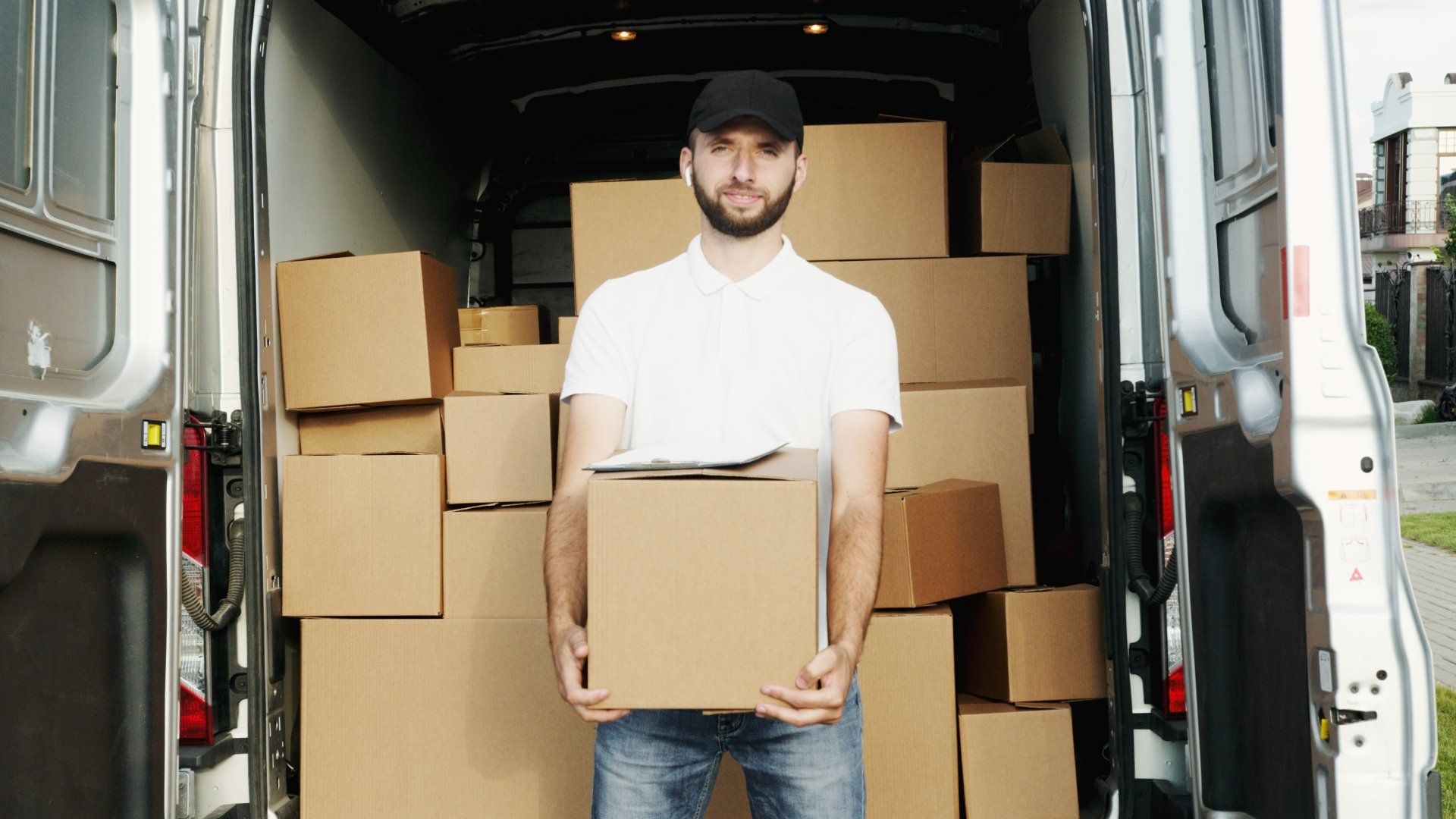 A delivery man is holding a cardboard box in front of a van filled with cardboard boxes.
