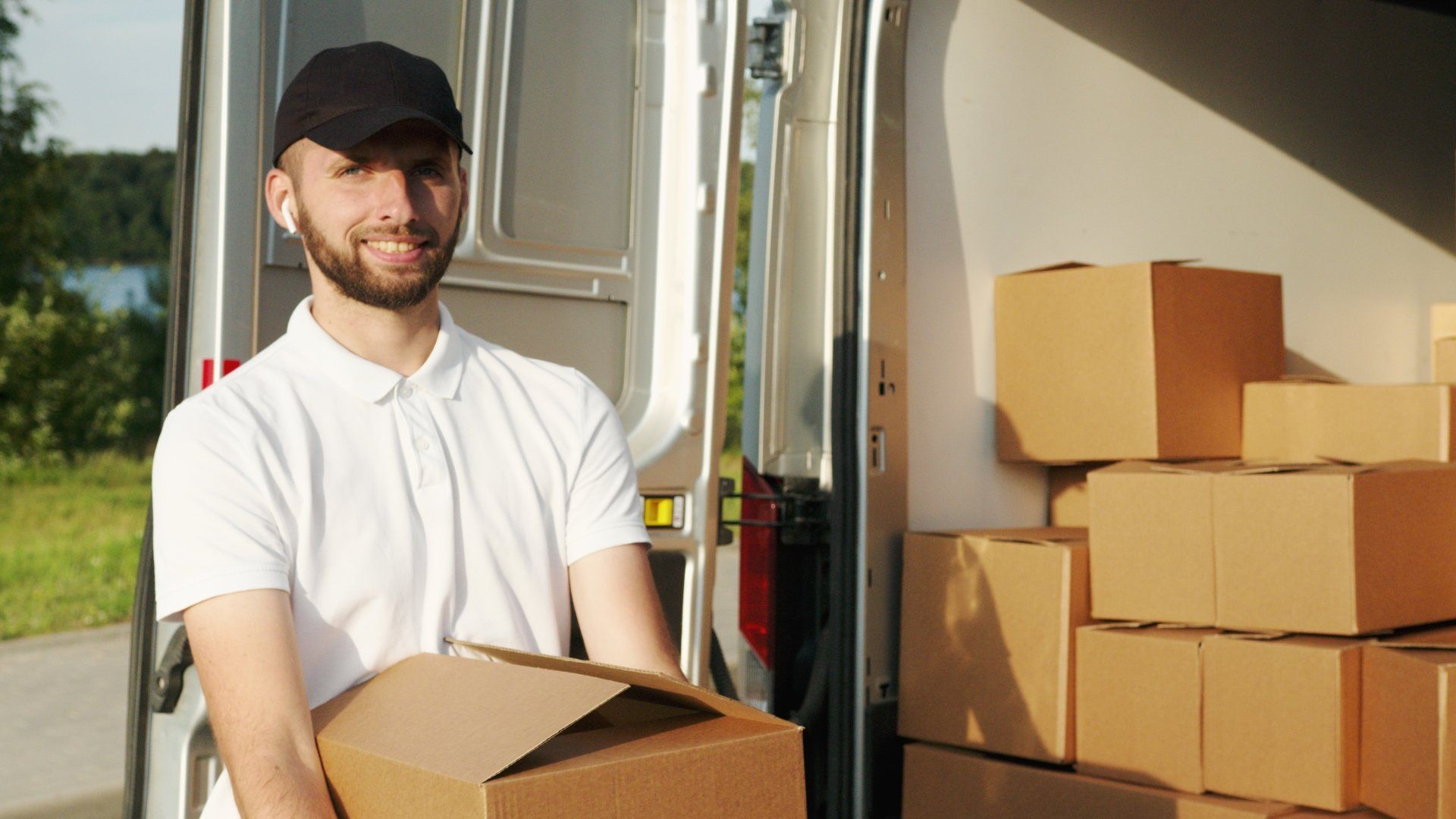 A delivery man is holding a box in front of a van filled with boxes.