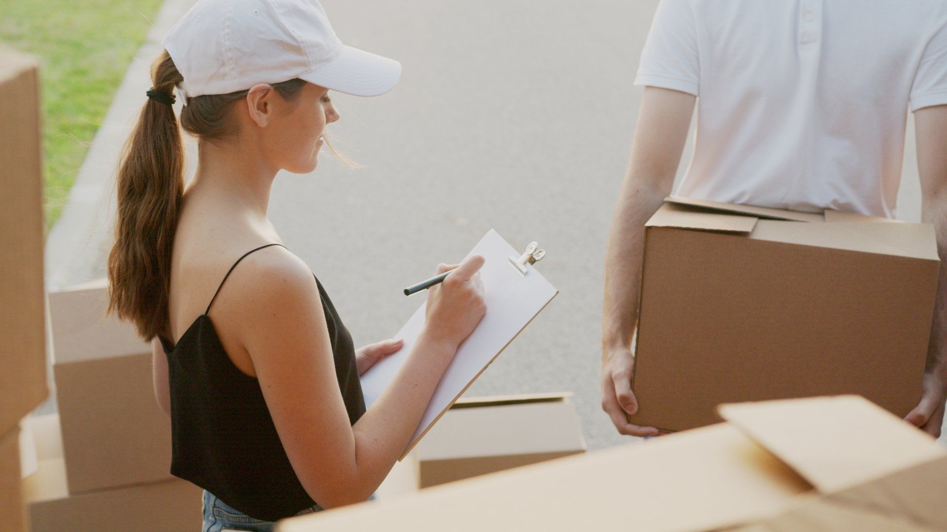 A woman is writing on a clipboard while a man holds a box.