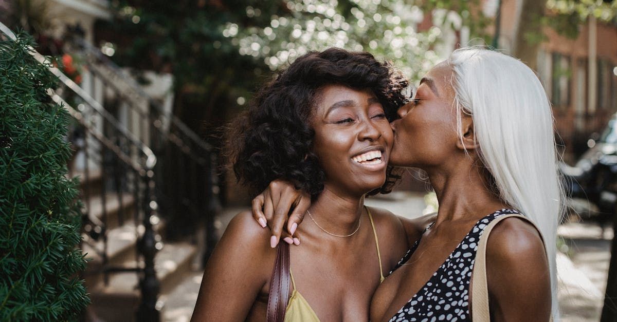 Two women outside and the woman on the right is kissing other woman check both are laughing