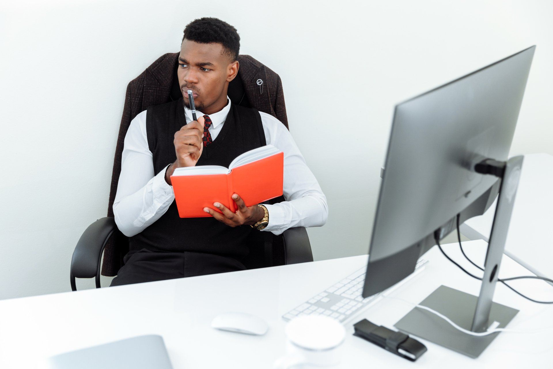 a man is sitting at a desk holding a book and a pen .