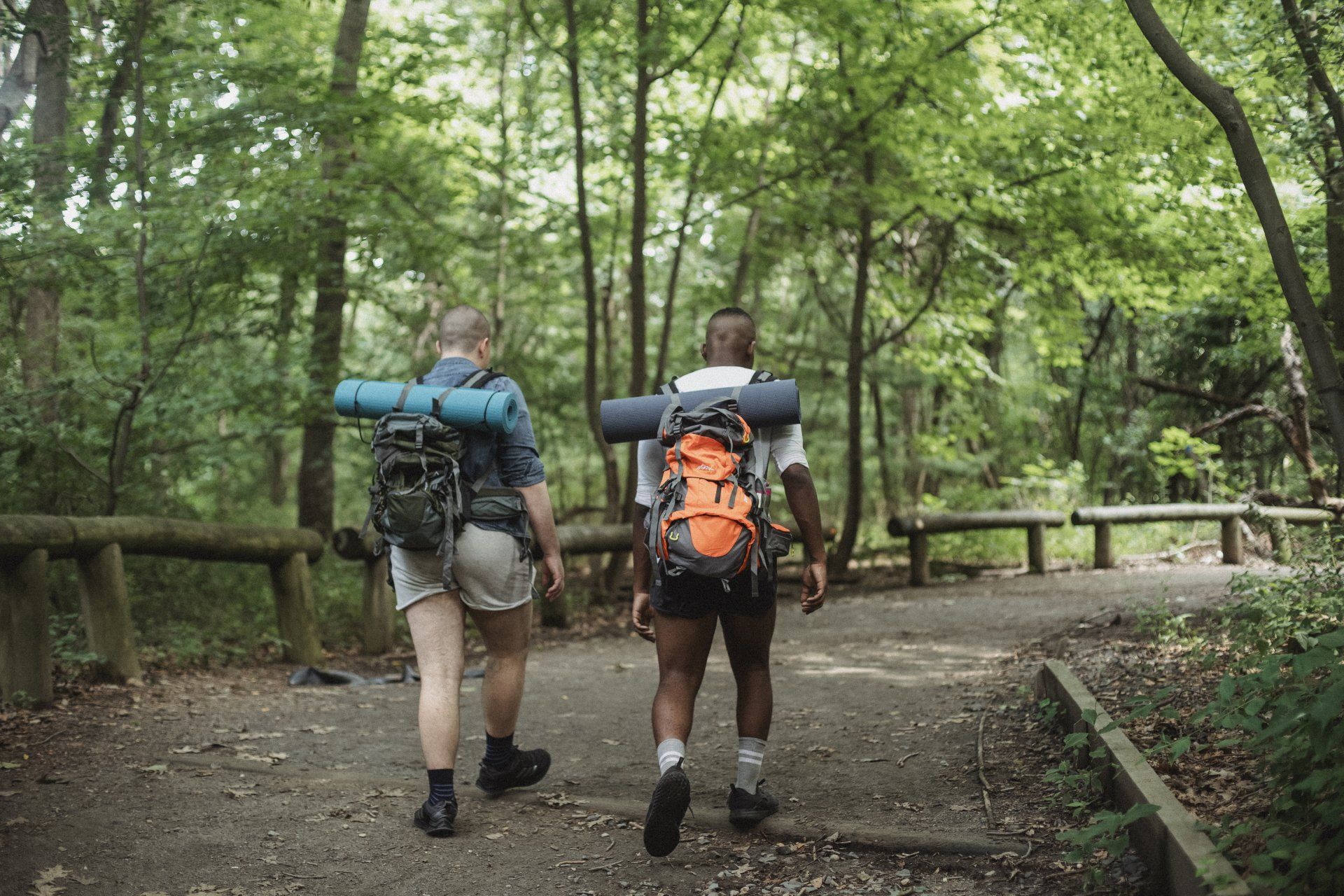 Two men with backpacks are walking down a path in the woods.