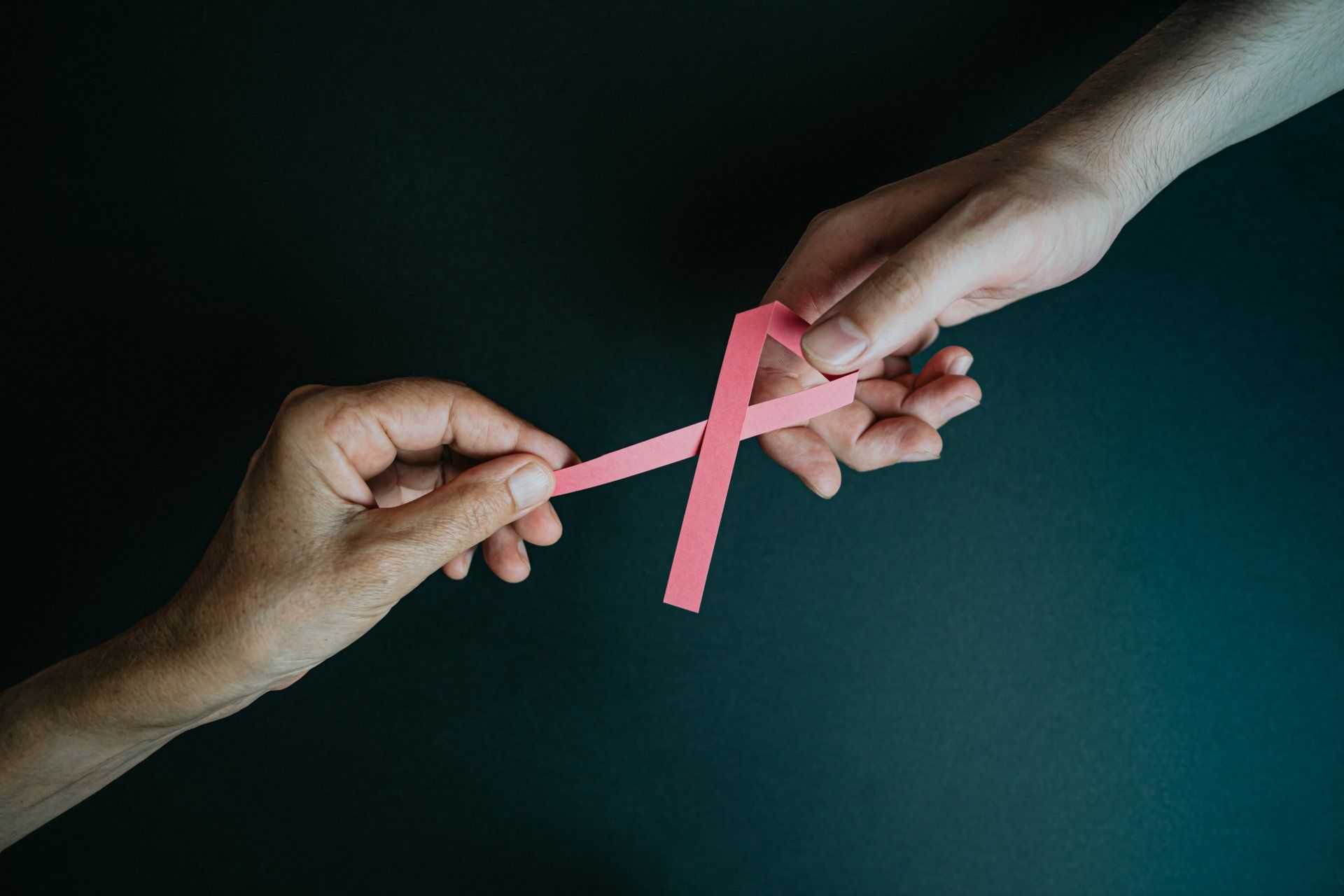 Two people are holding a pink ribbon in their hands.