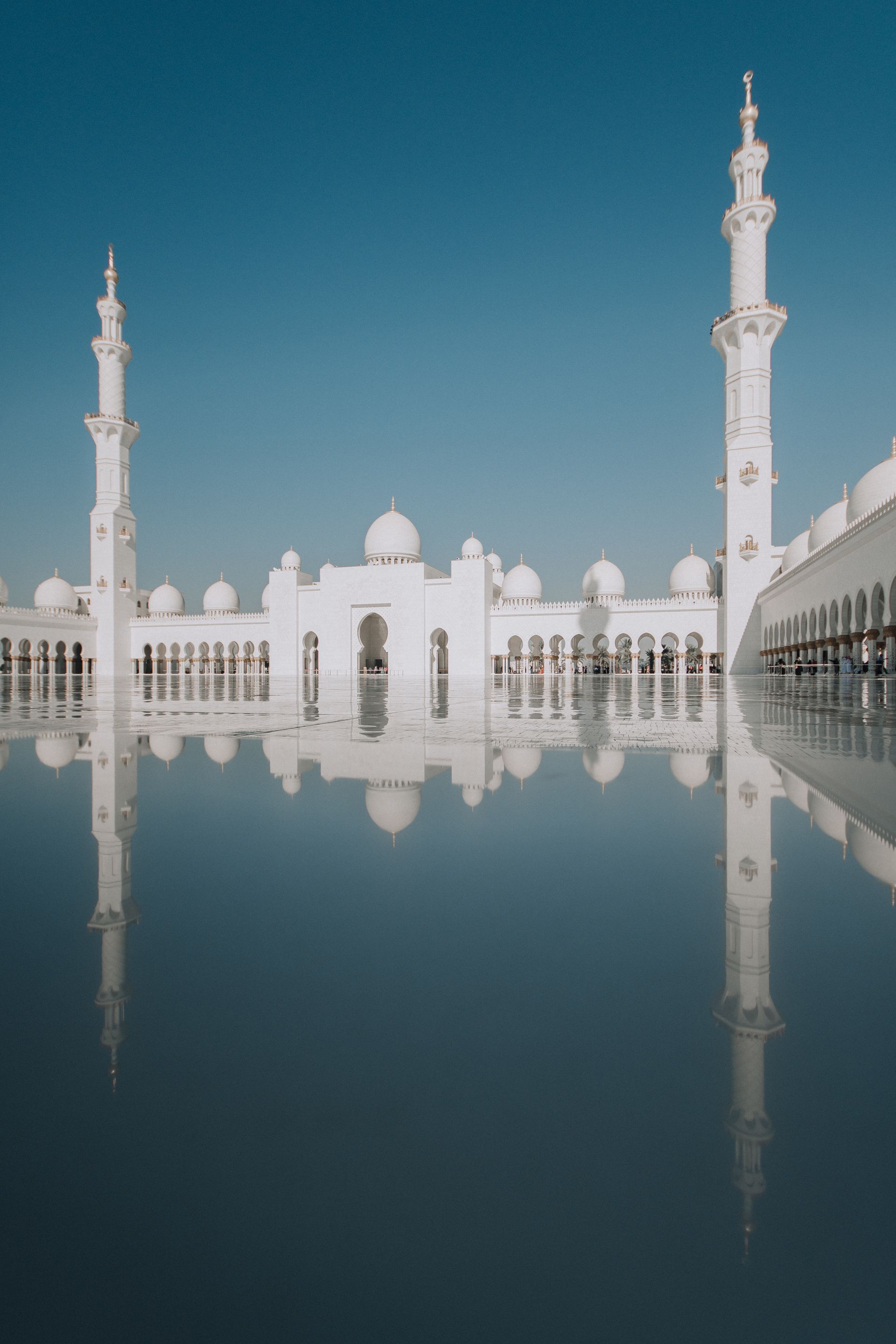 A white mosque with two minaret 's is reflected in the water.