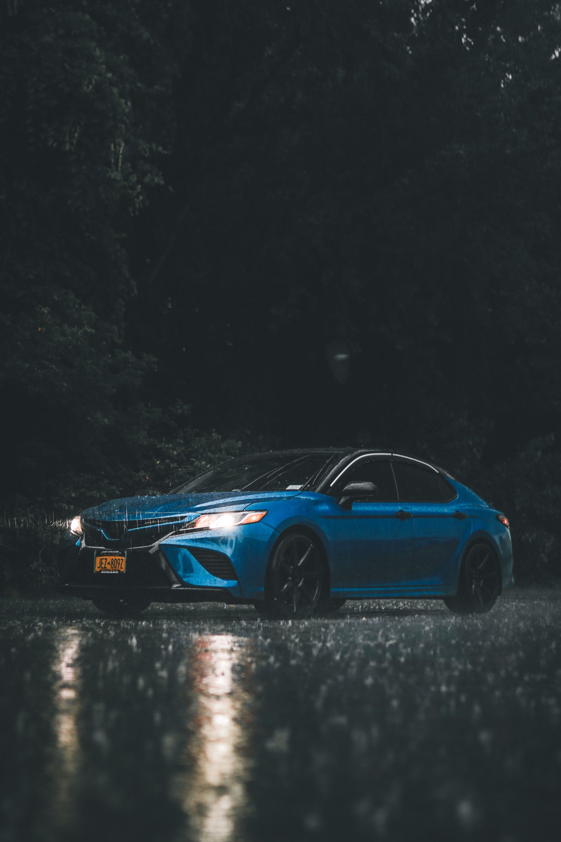 A blue car is driving down a wet road in the rain.