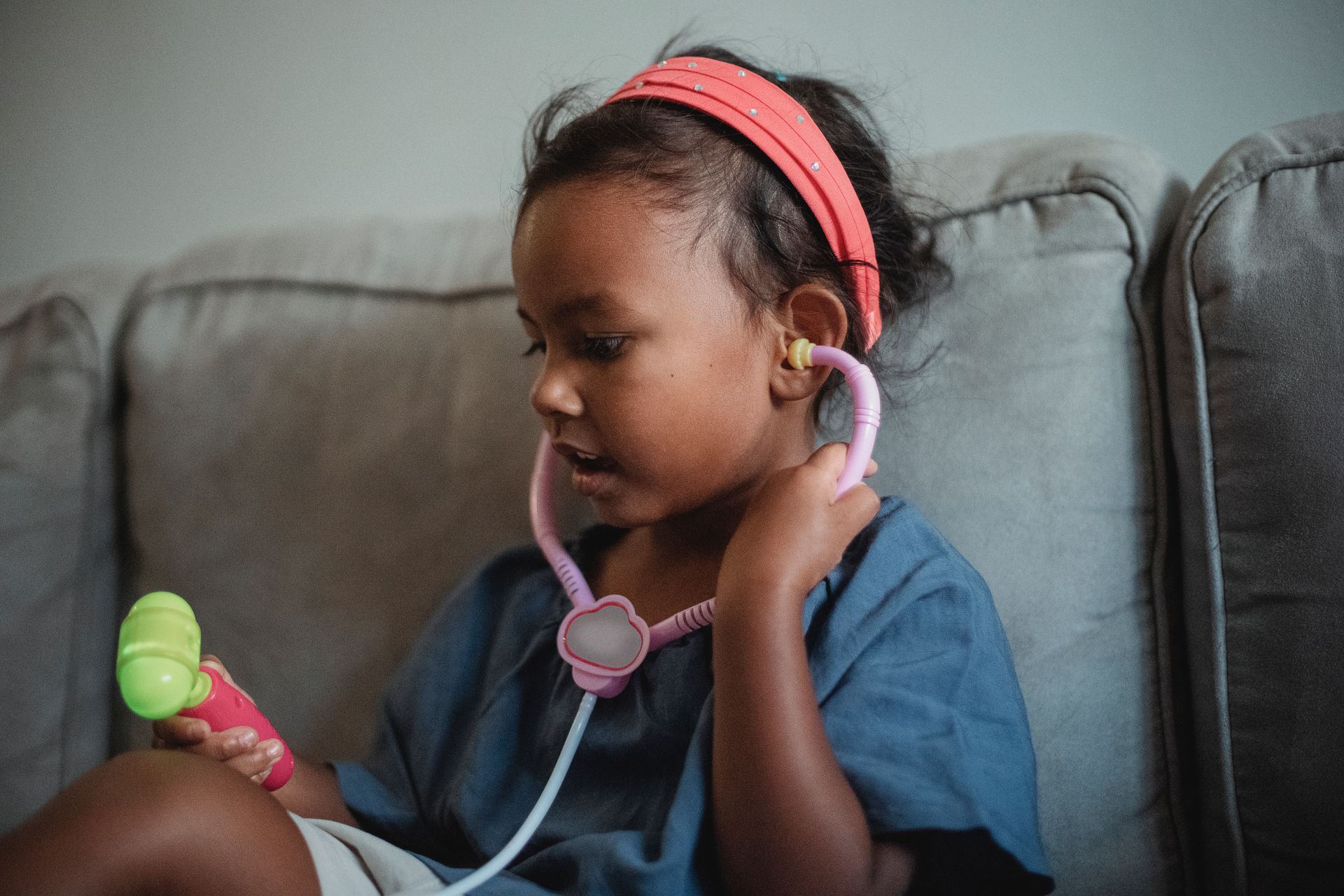 Child playing doctor with a stethoscope and toy instrument on a sofa.