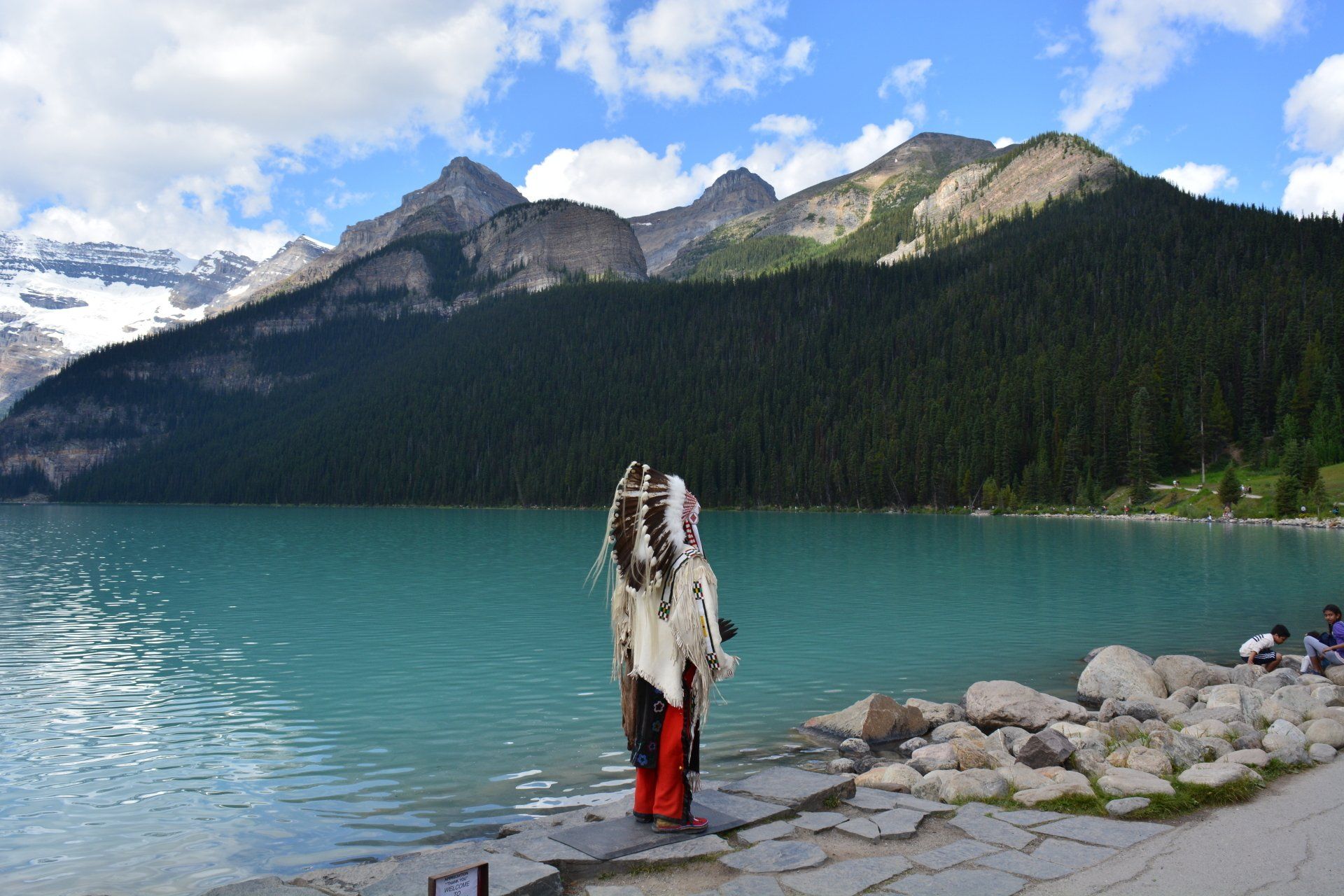 Native man with feather head dress water mountains sky
