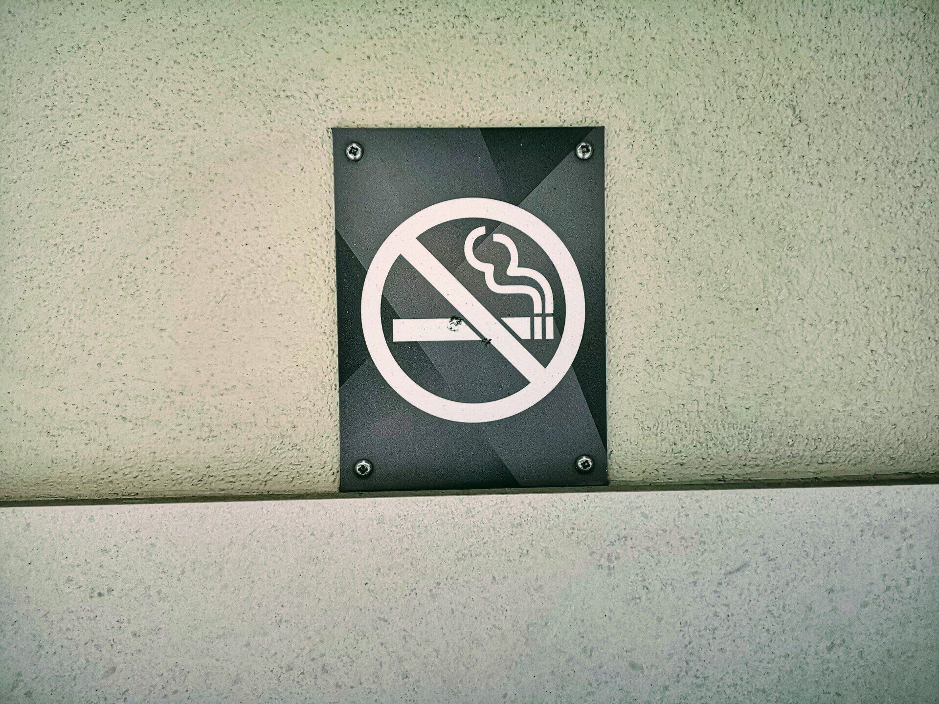 No smoking sign on a dark plaque mounted on a light wall.