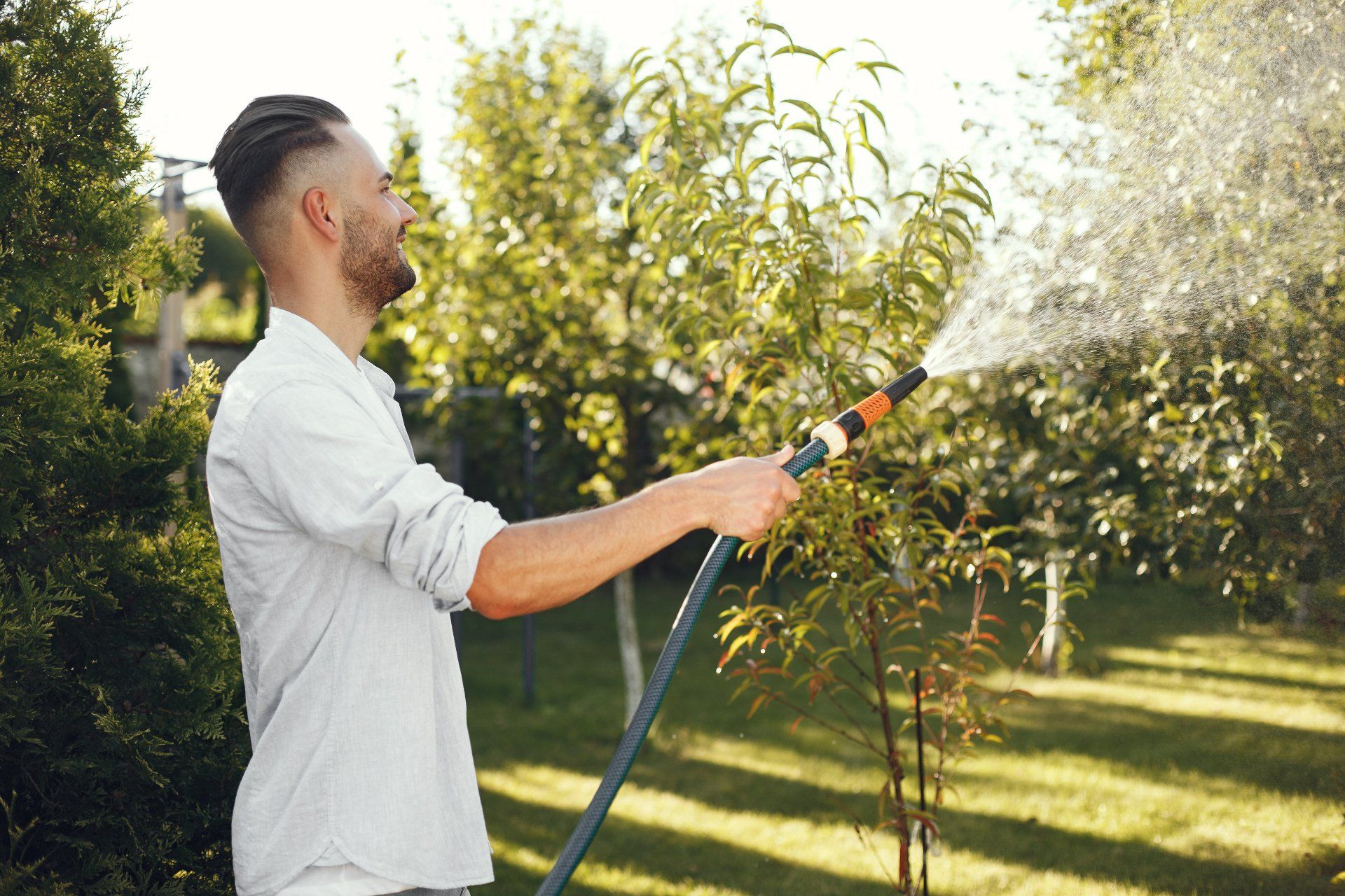 A young man holding a hose and spraying his lawn