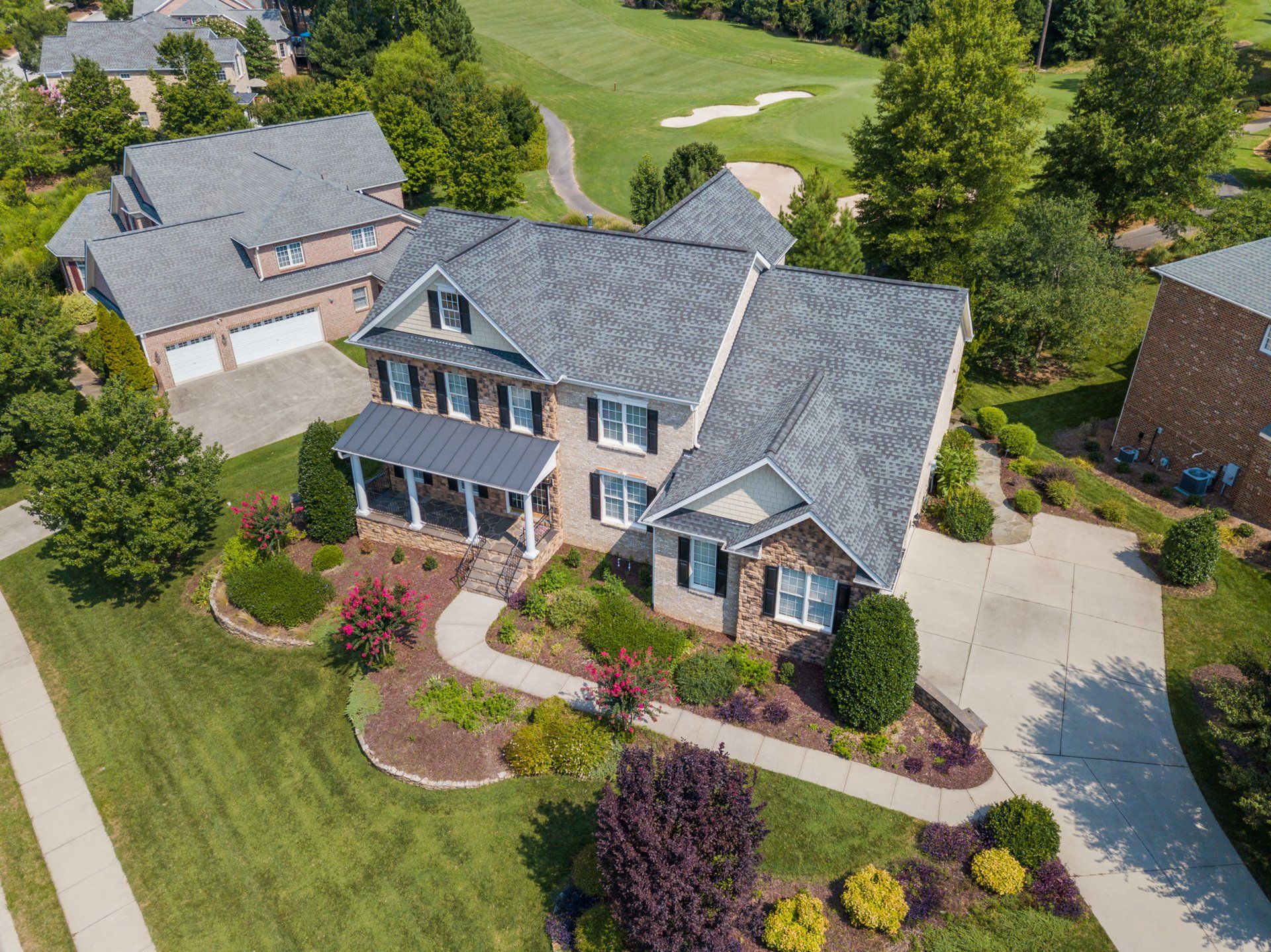 Aerial view of a two-story brick home with a gray roof and a well-manicured yard next to a golf course.