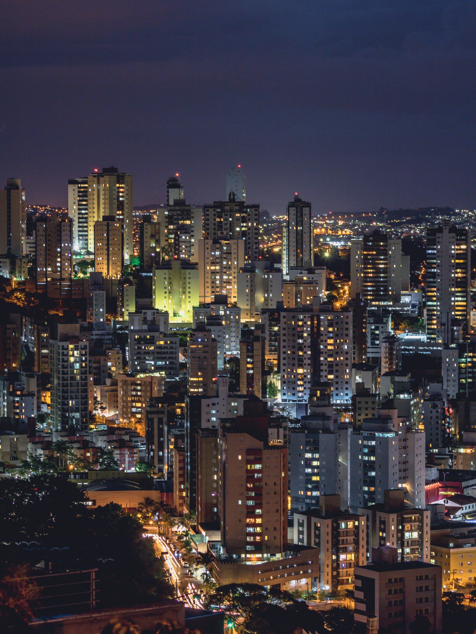 Vista da cidade à noite, edifícios iluminados sob um céu azul escuro.