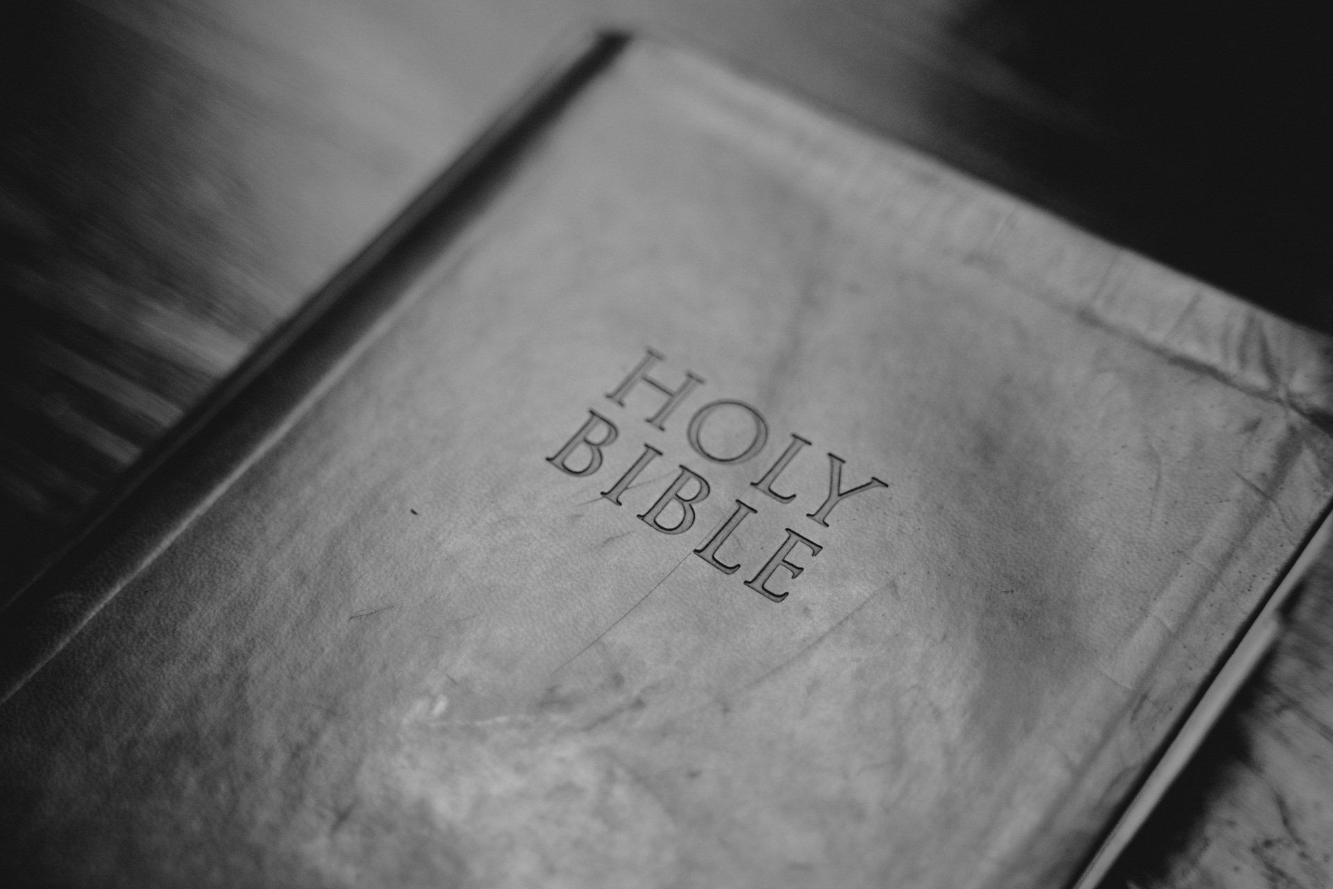 A black and white photo of a holy bible on a table.