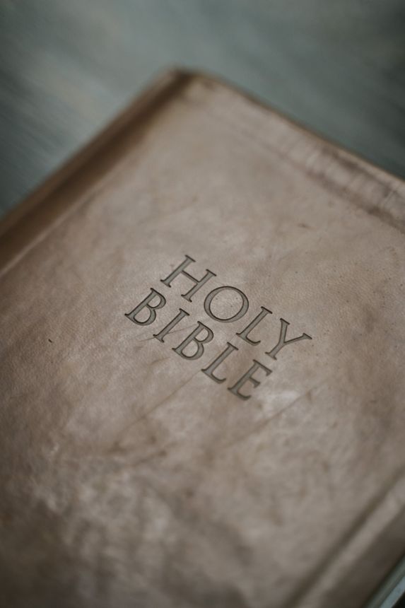 A worn Holy Bible with a brown cover lying on a soft gray surface.