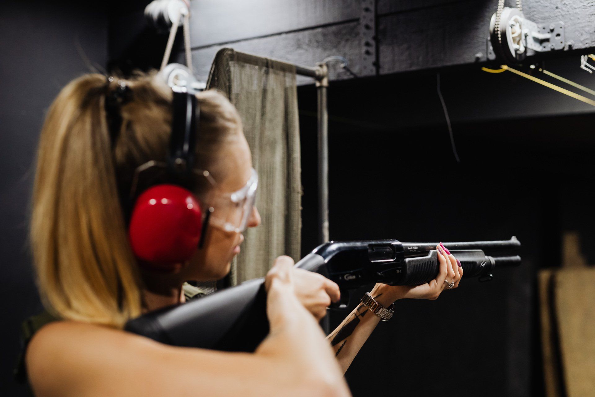 Person wearing red earmuffs and safety glasses aims a handgun at an indoor shooting range