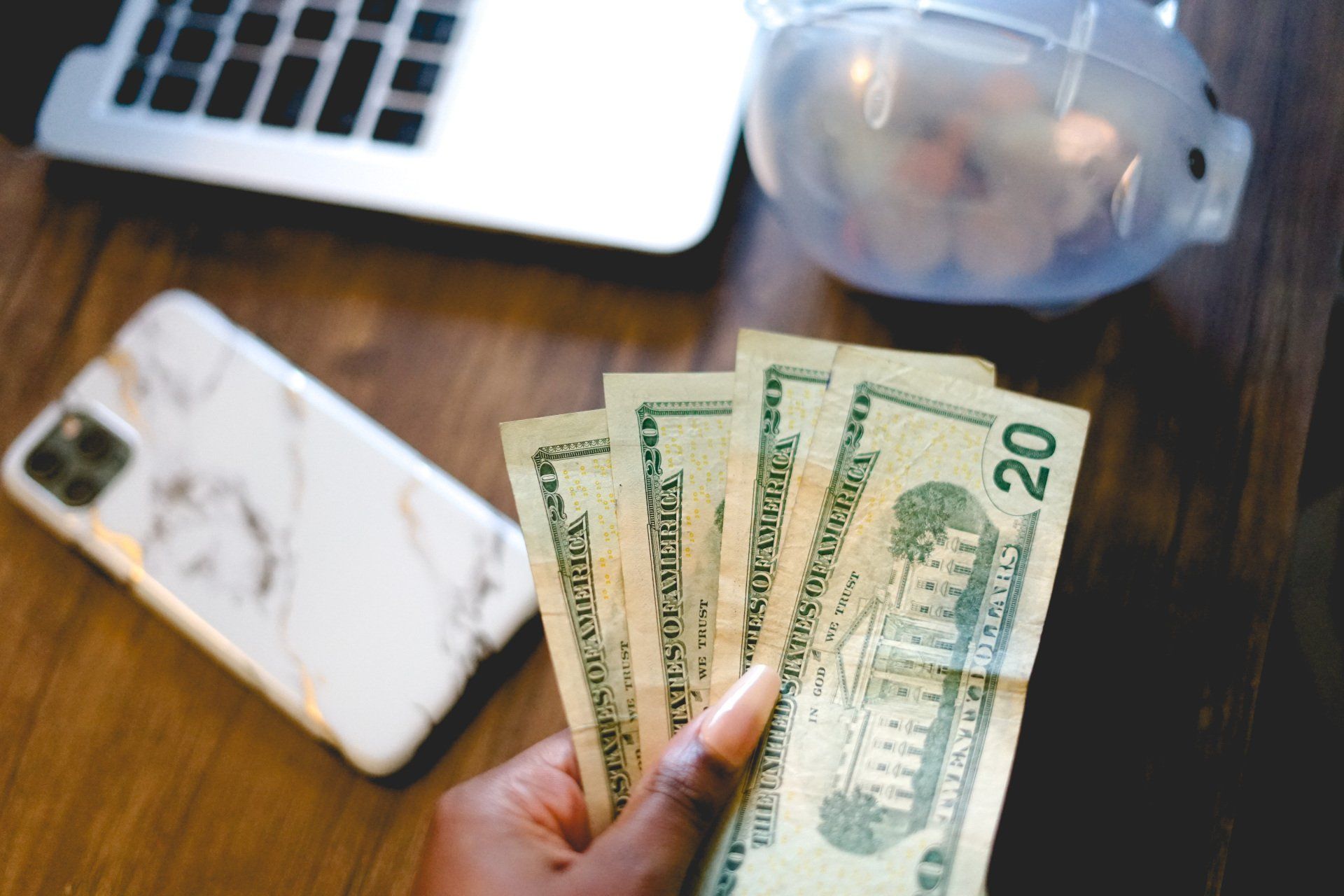 A person is holding a bunch of money in front of a laptop and a piggy bank.