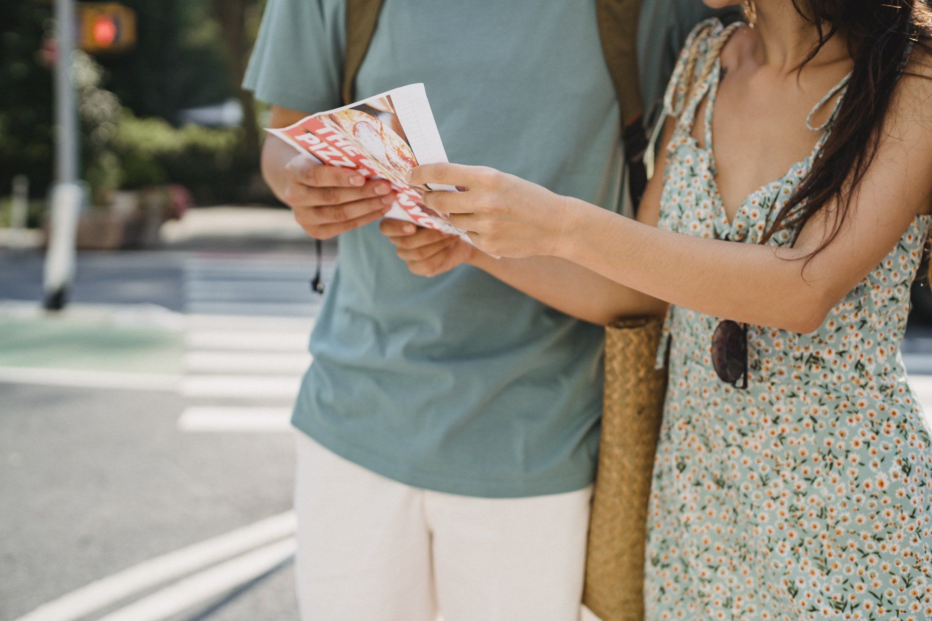 Two people study a folded map beside a street, one in a patterned dress holding it up.