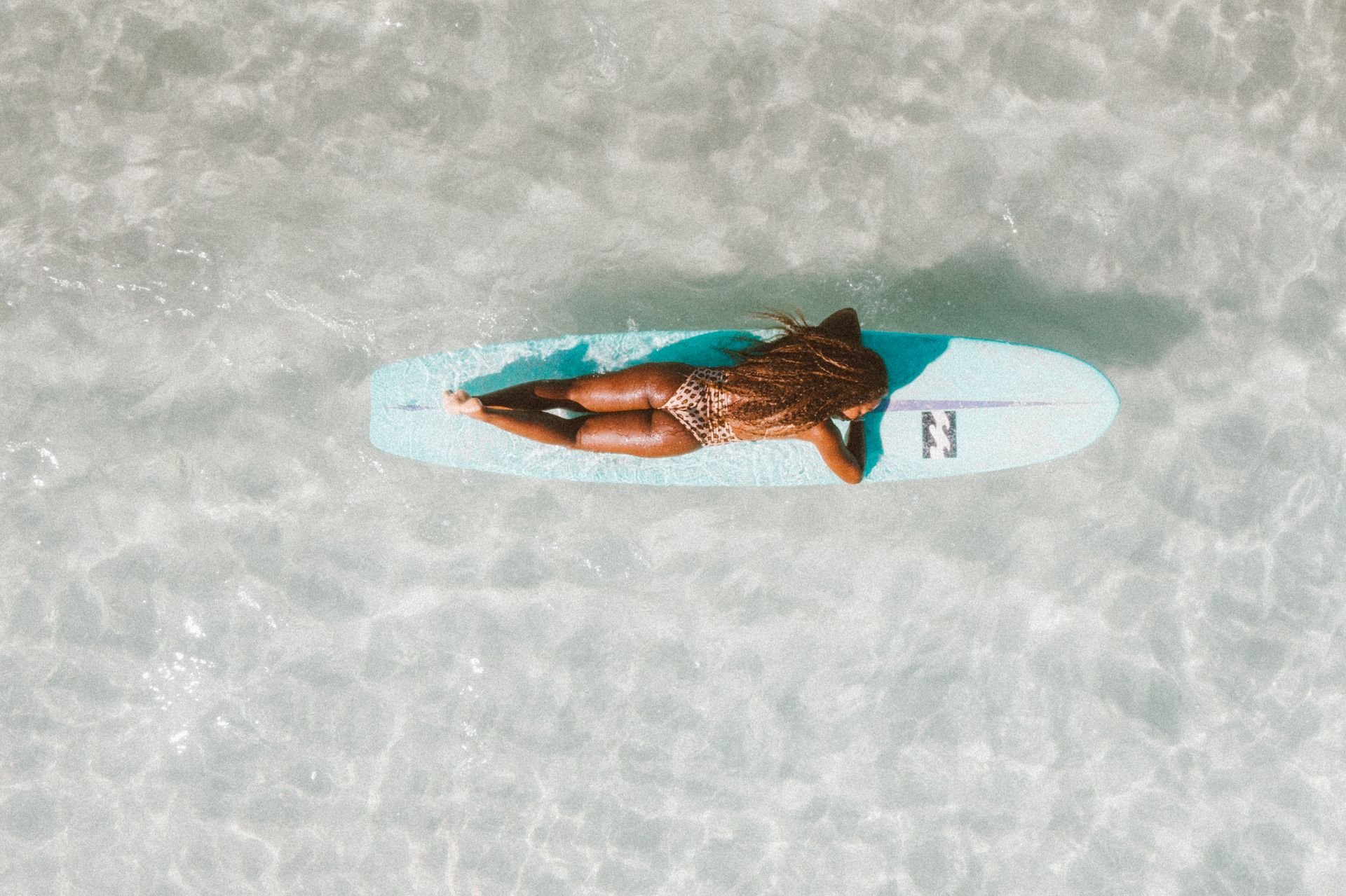 Person on a light blue surfboard floats in clear, turquoise water.