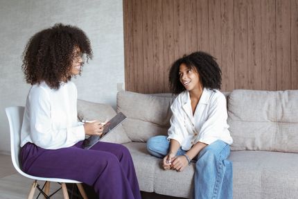 Two women are sitting on a couch talking to each other.